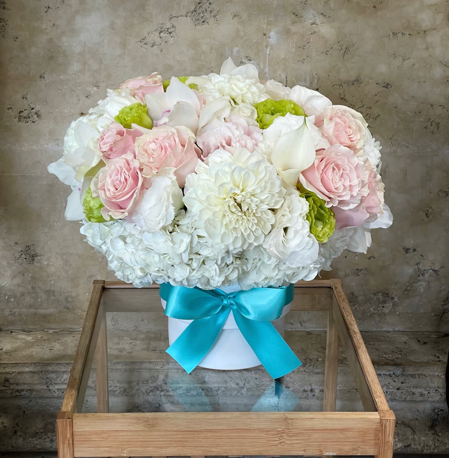 Pink and white flower arrangement in a white box with a blue ribbon
