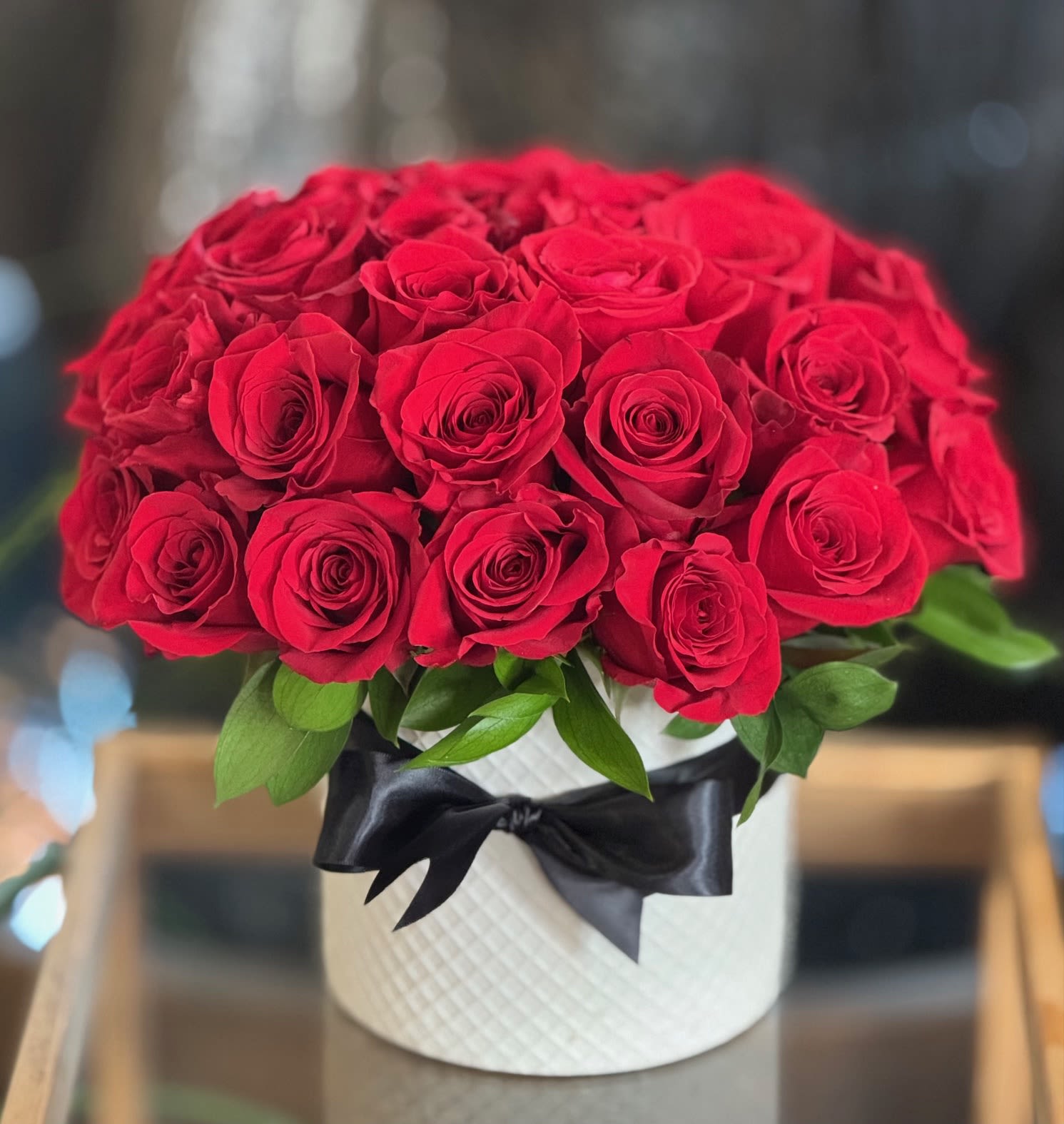 Red roses arranged in a white hatbox with a black ribbon