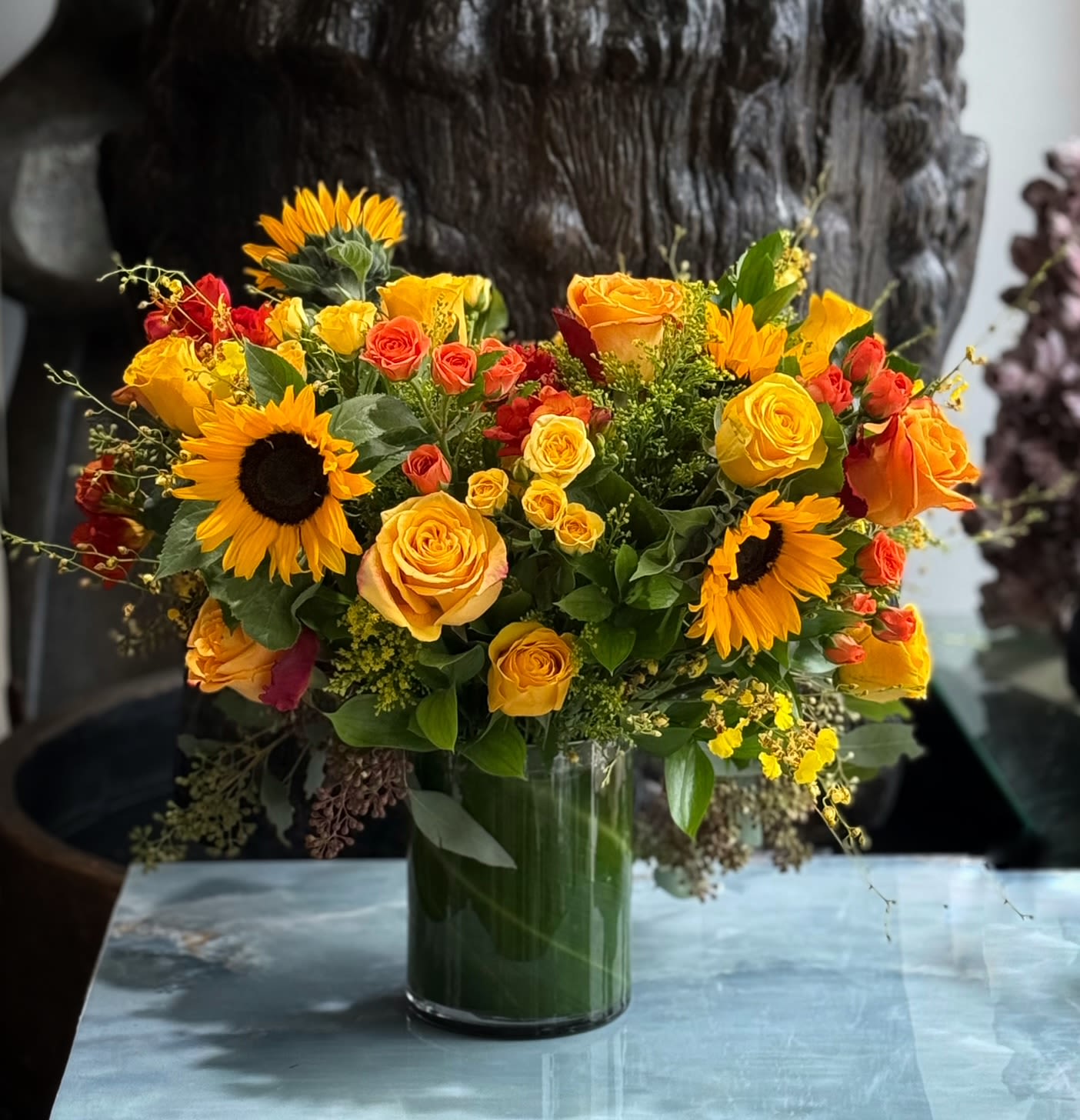 Bouquet of yellow and orange roses with sunflowers in a glass vase