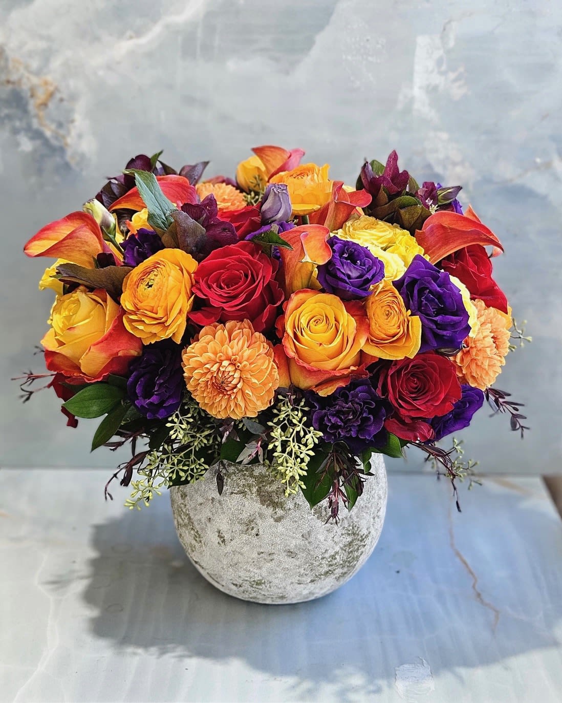 Mixed bouquet of roses, calla lilies, and dahlias in a stone vase