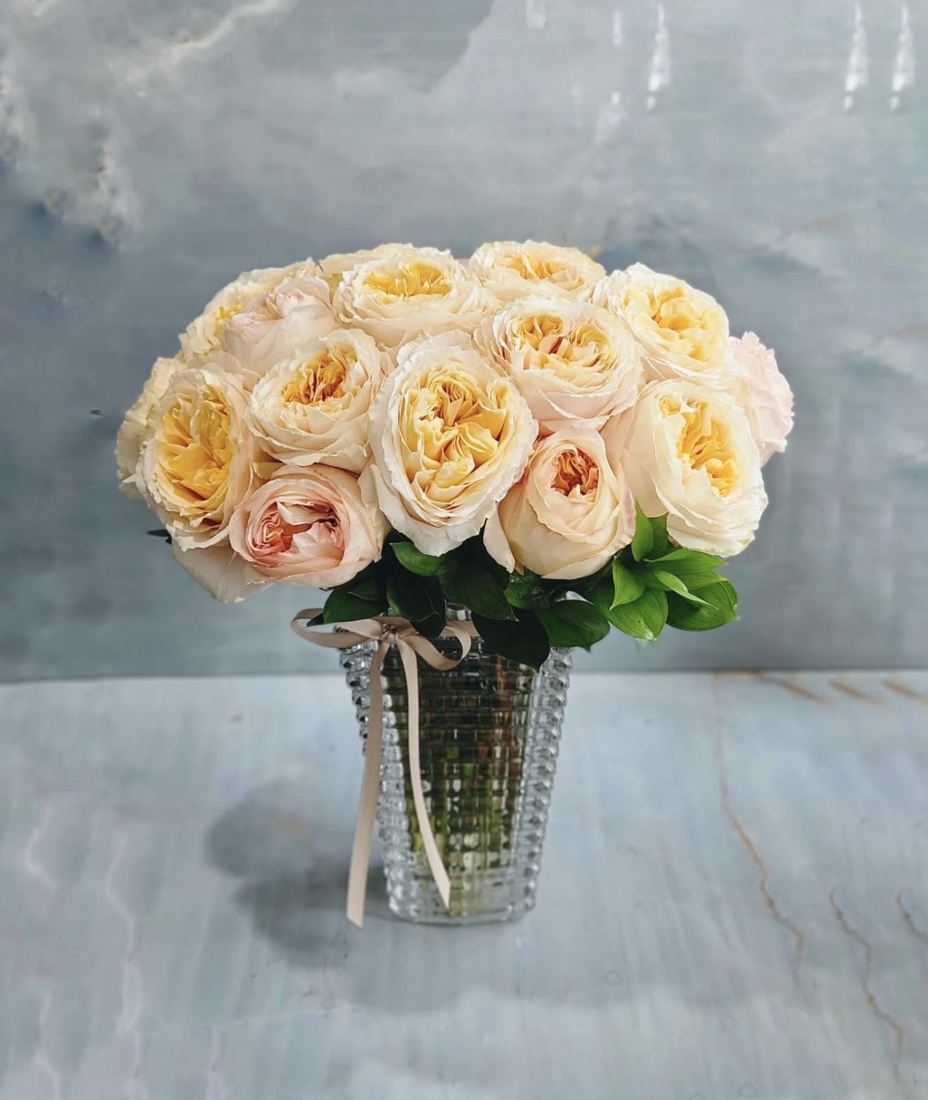 Peach and cream roses in a clear glass vase with a ribbon