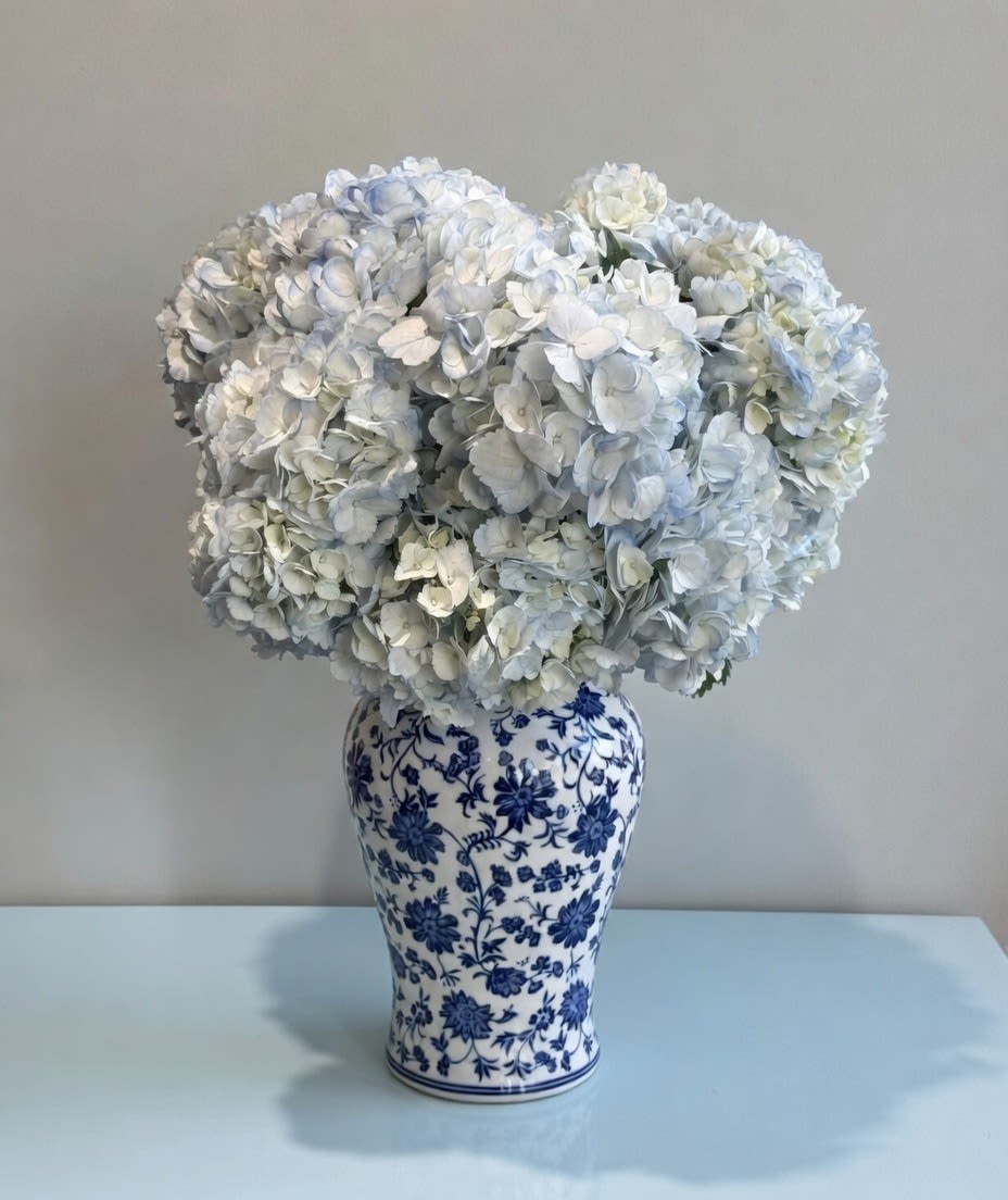 Blue Sky - This arrangement is effortlessly elegant, pairing voluminous pale blue hydrangeas with the timeless charm of a blue-and-white chinoiserie vase. The monochromatic palette evokes the serenity of a coastal garden, while the abundant blooms create a full, cloud-like silhouette that is both classic and luxurious. 