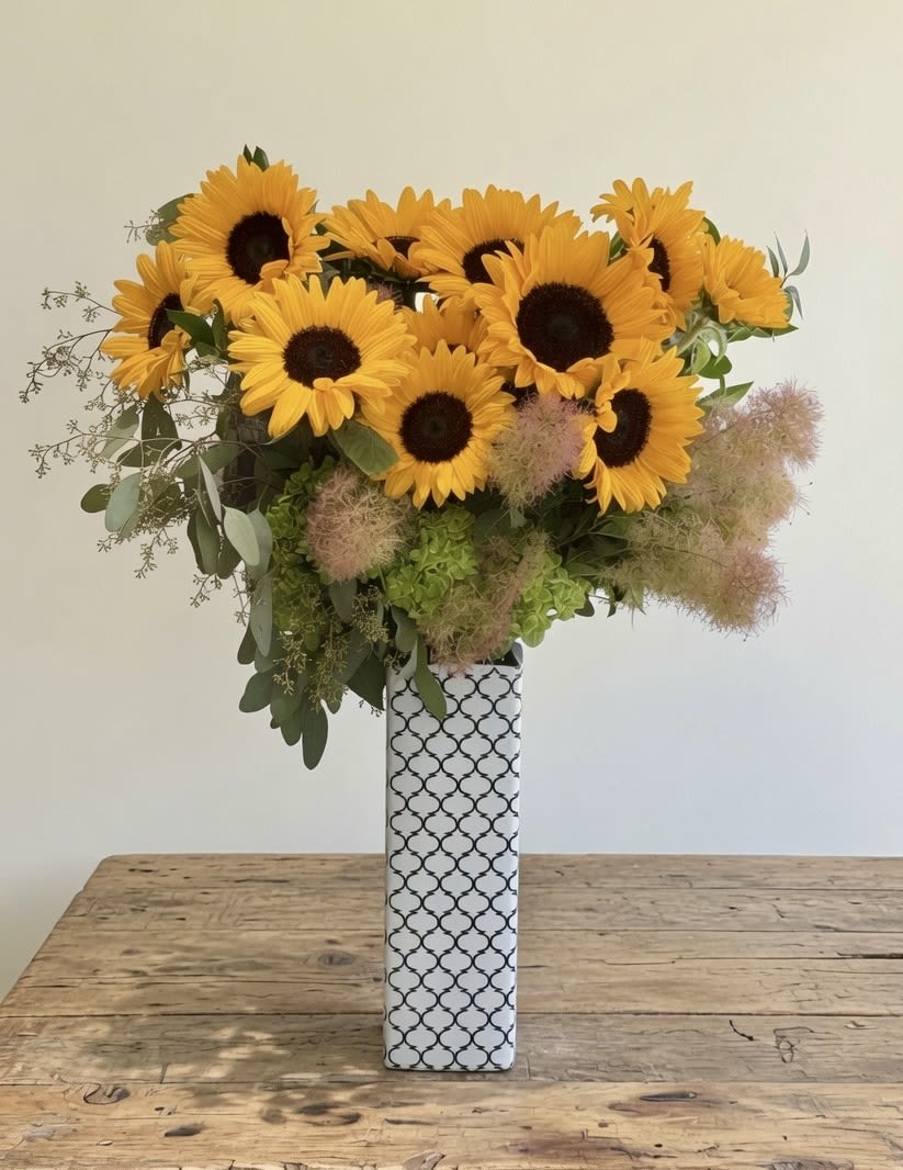 Rising Sun  - This arrangement is bright, cheerful, and effortlessly elegant. Golden sunflowers take center stage, their bold faces complemented by airy smoke bush, fresh green hydrangeas, and soft eucalyptus.  