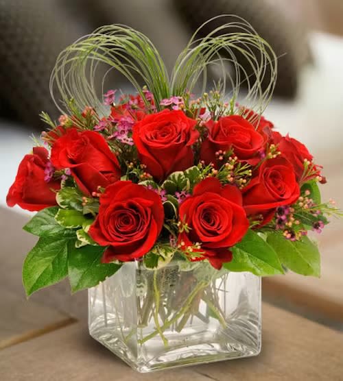 Red roses arranged in a clear square glass vase with decorative loops
