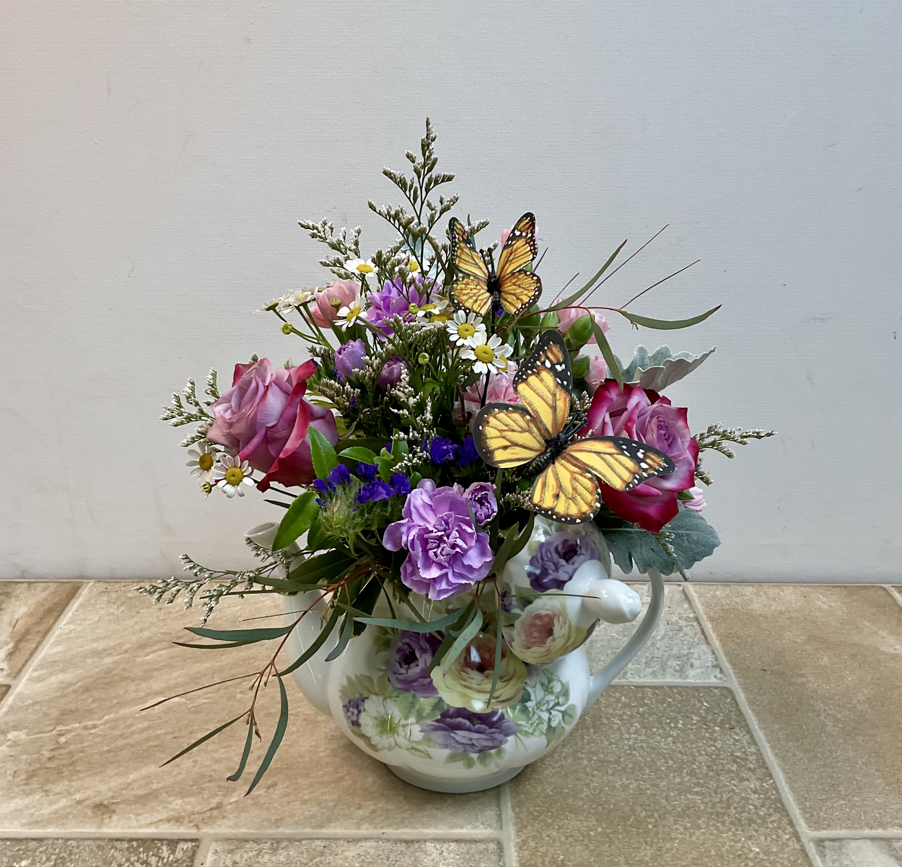 Pink and purple flowers arranged in a floral teapot with butterfly picks
