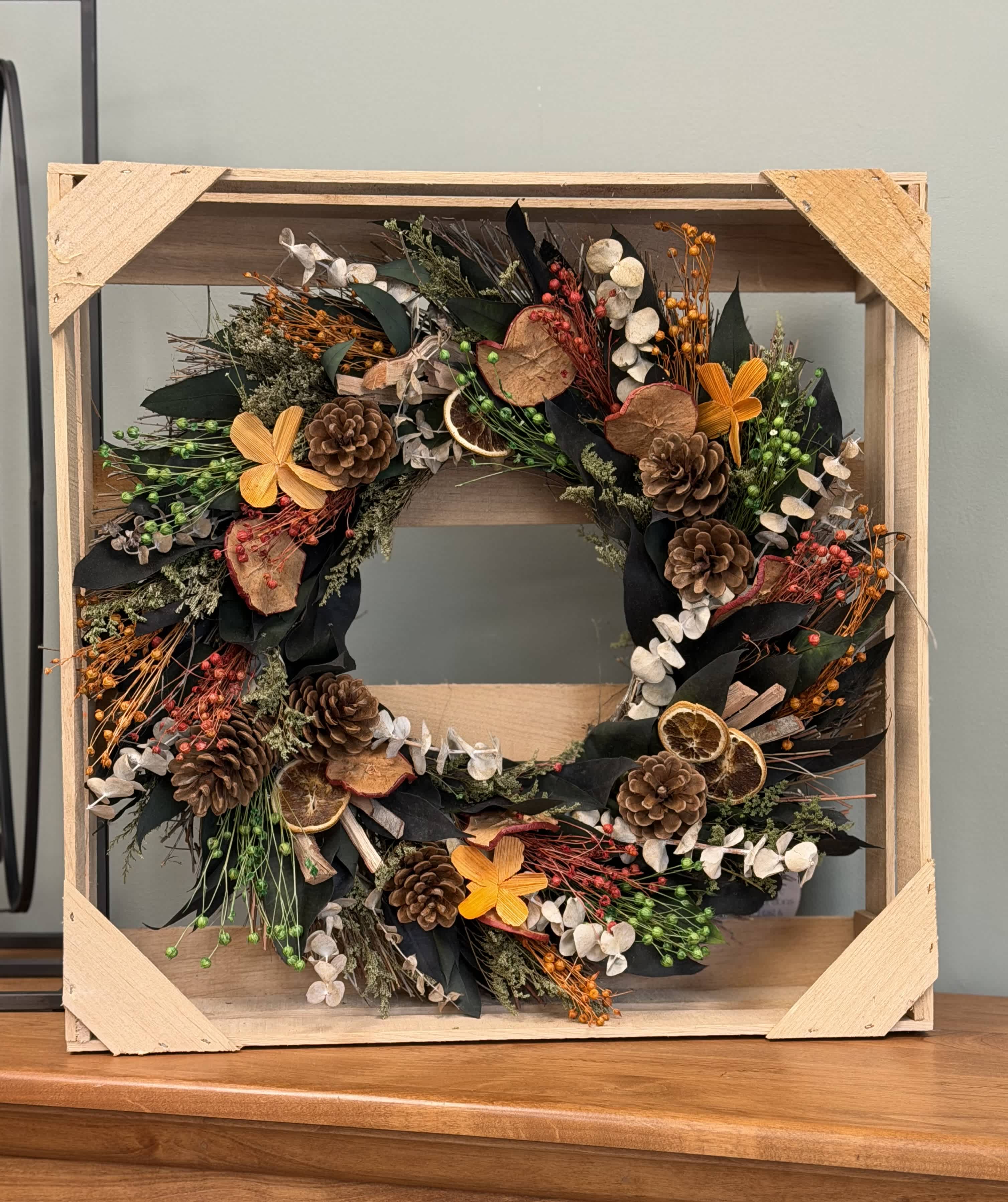 Rustic wreath with pinecones, dried orange slices, and orange flowers in a wooden frame