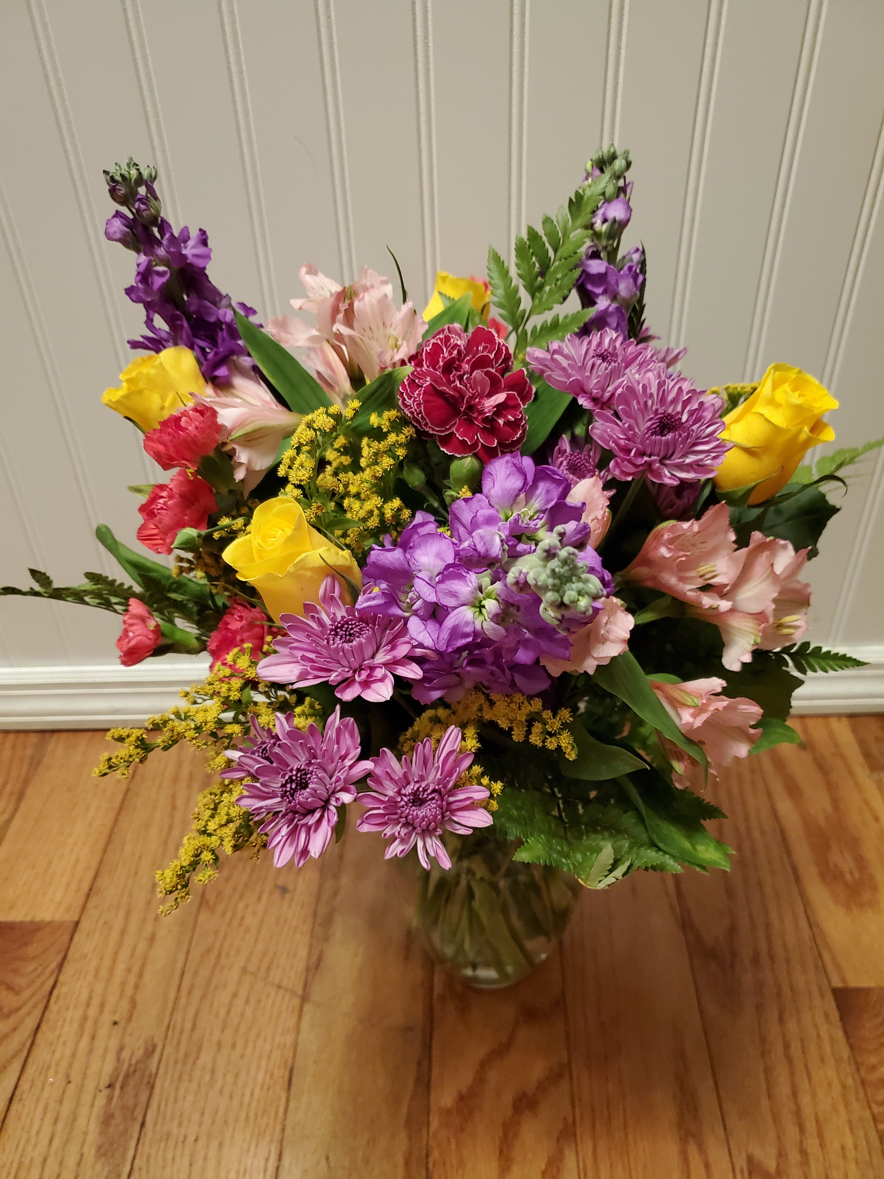 Mixed bouquet of yellow roses, purple mums, pink alstroemeria and carnations in a clear glass vase