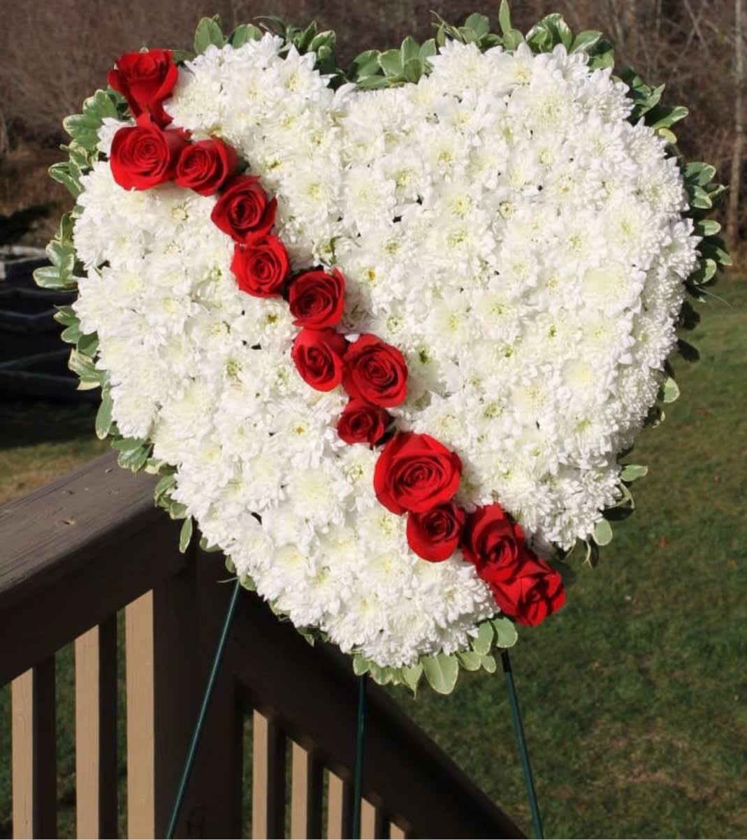 Heart-shaped standing wreath of white flowers with a diagonal line of red roses.
