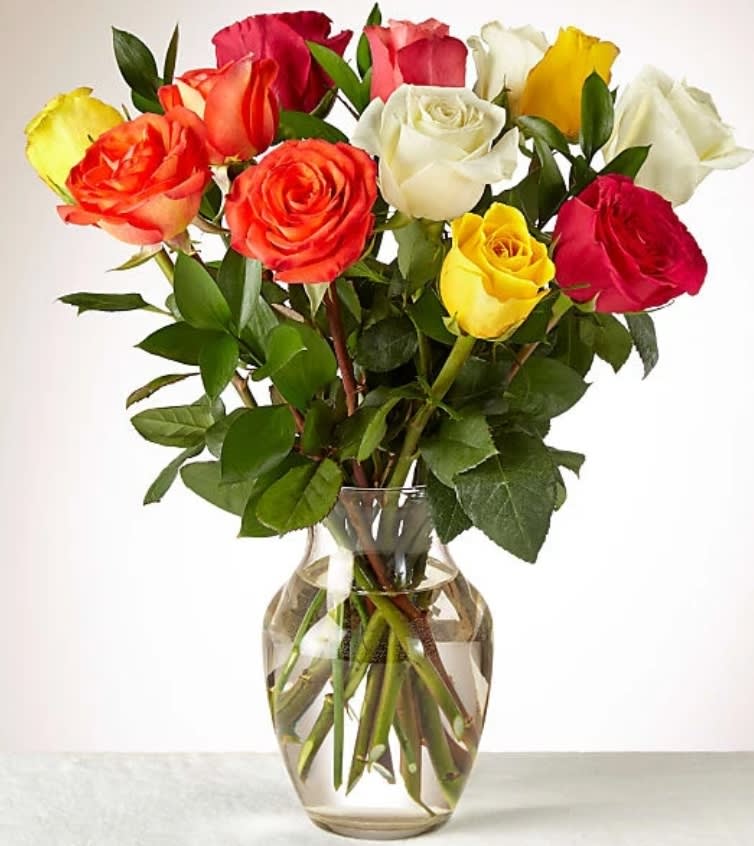 Mixed bouquet of red, yellow, white, and orange roses arranged in a clear glass vase