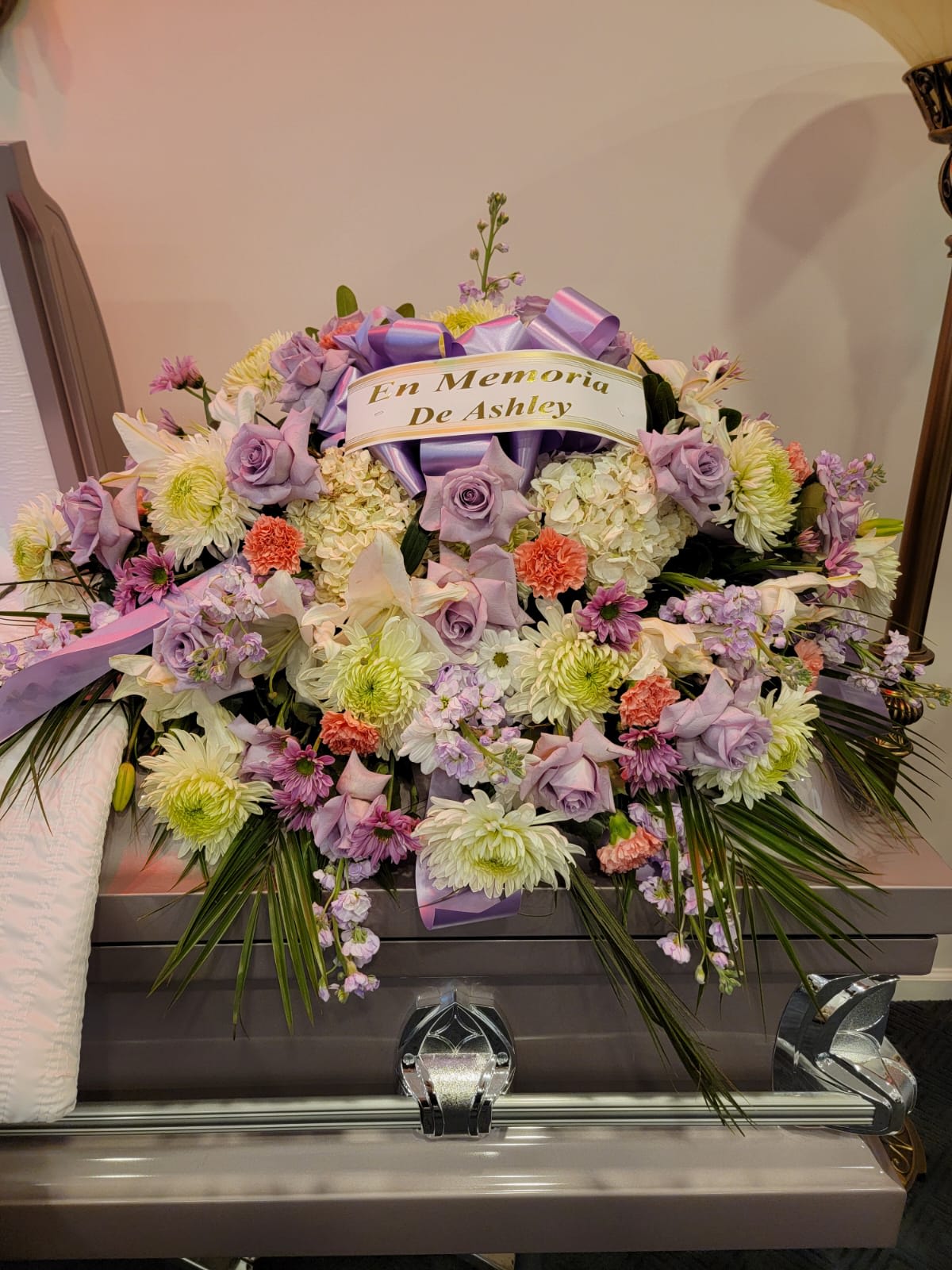 Casket spray of lavender roses, white mums, and mixed blooms with a memorial ribbon