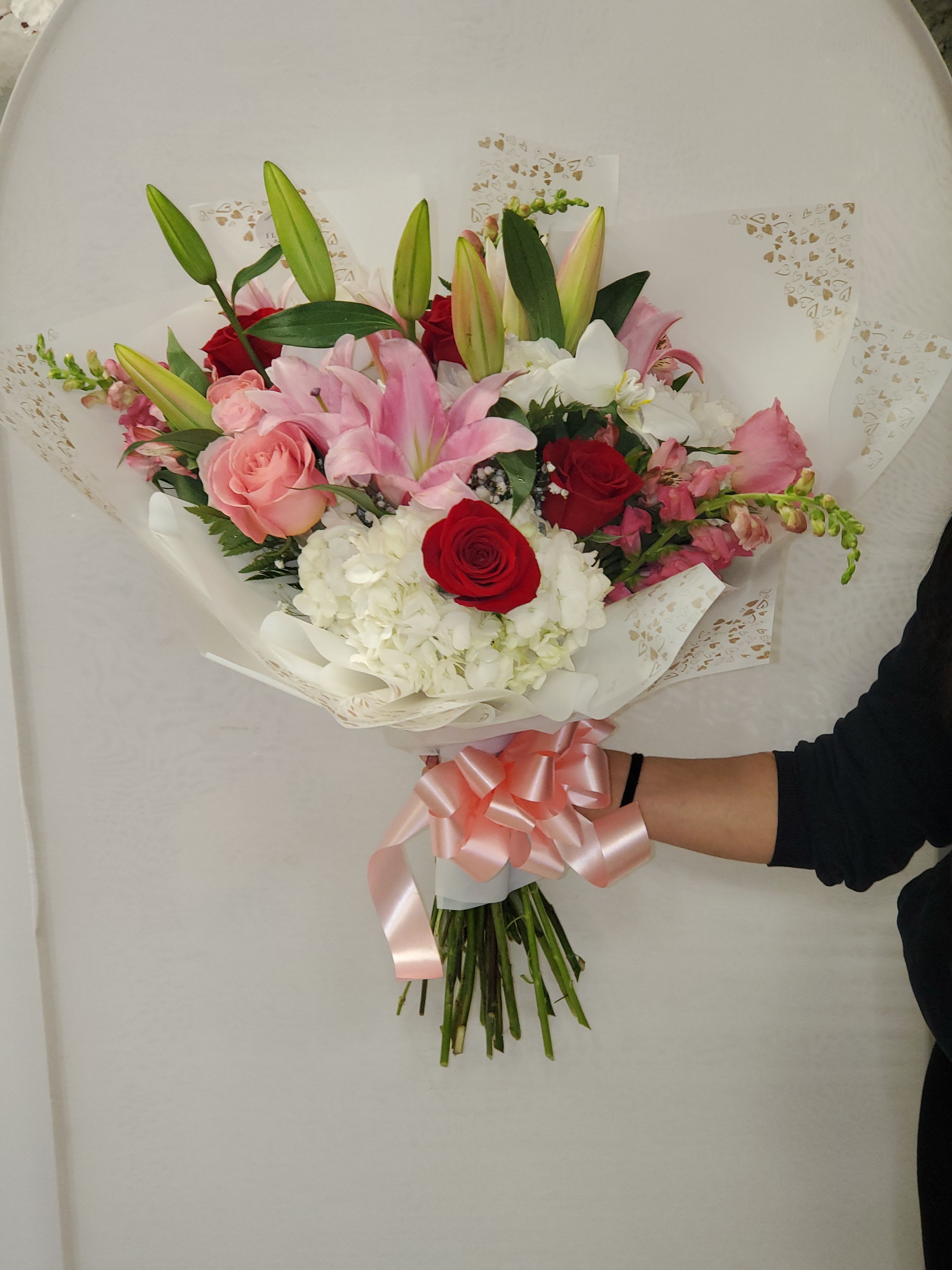 Hand-tied bouquet of pink lilies, roses, and white hydrangeas wrapped with pink ribbon.