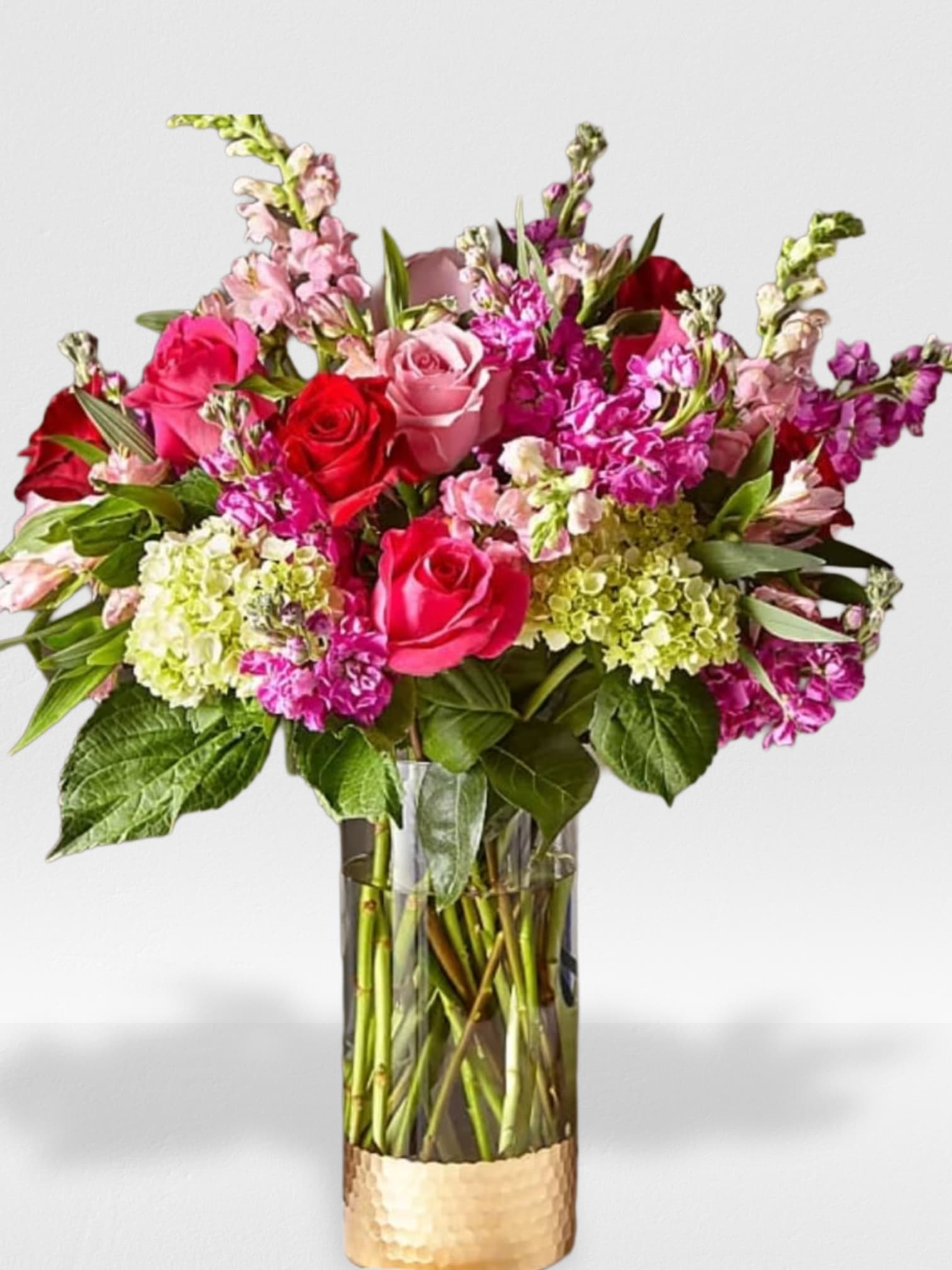 Tall arrangement of pink and red roses, pink snapdragons, and green hydrangeas in a glass vase