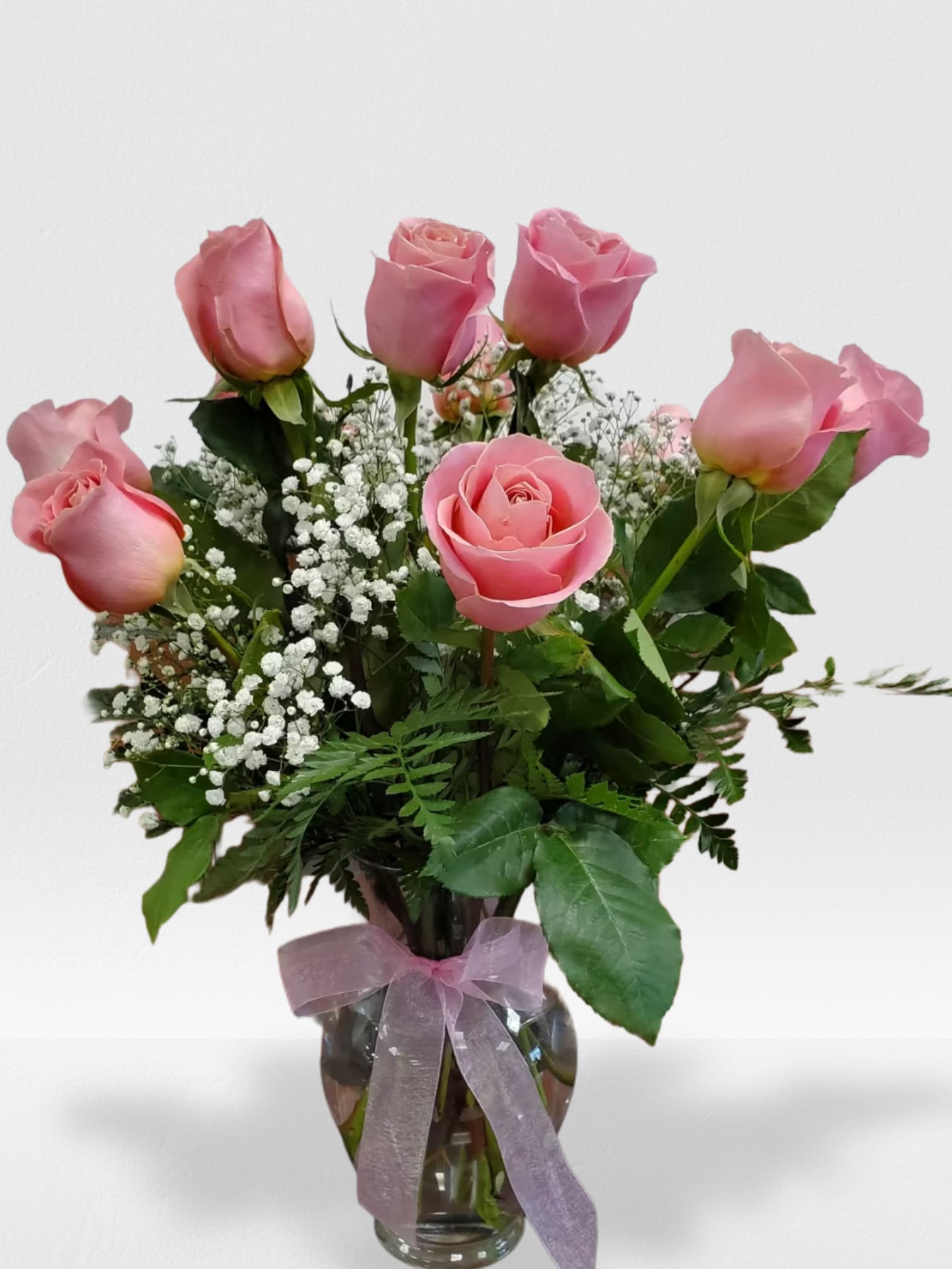 Glass vase of pink roses with white filler flowers and a pink ribbon bow