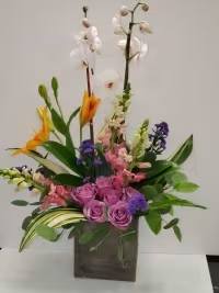 Tall mixed floral arrangement in a dark square vase with pink, purple, white, and orange blooms