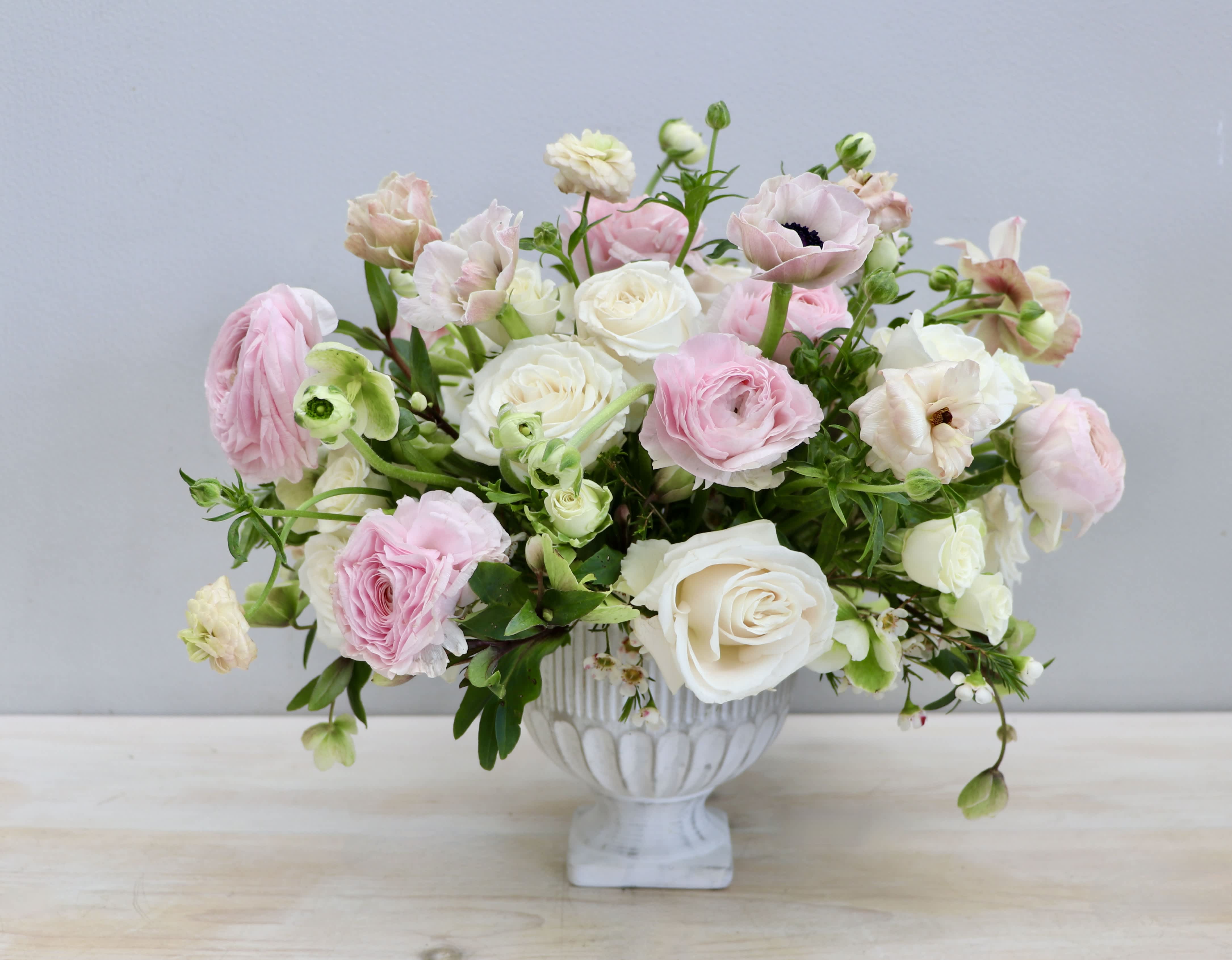 Low arrangement of pink and ivory roses and ranunculus in a white pedestal bowl