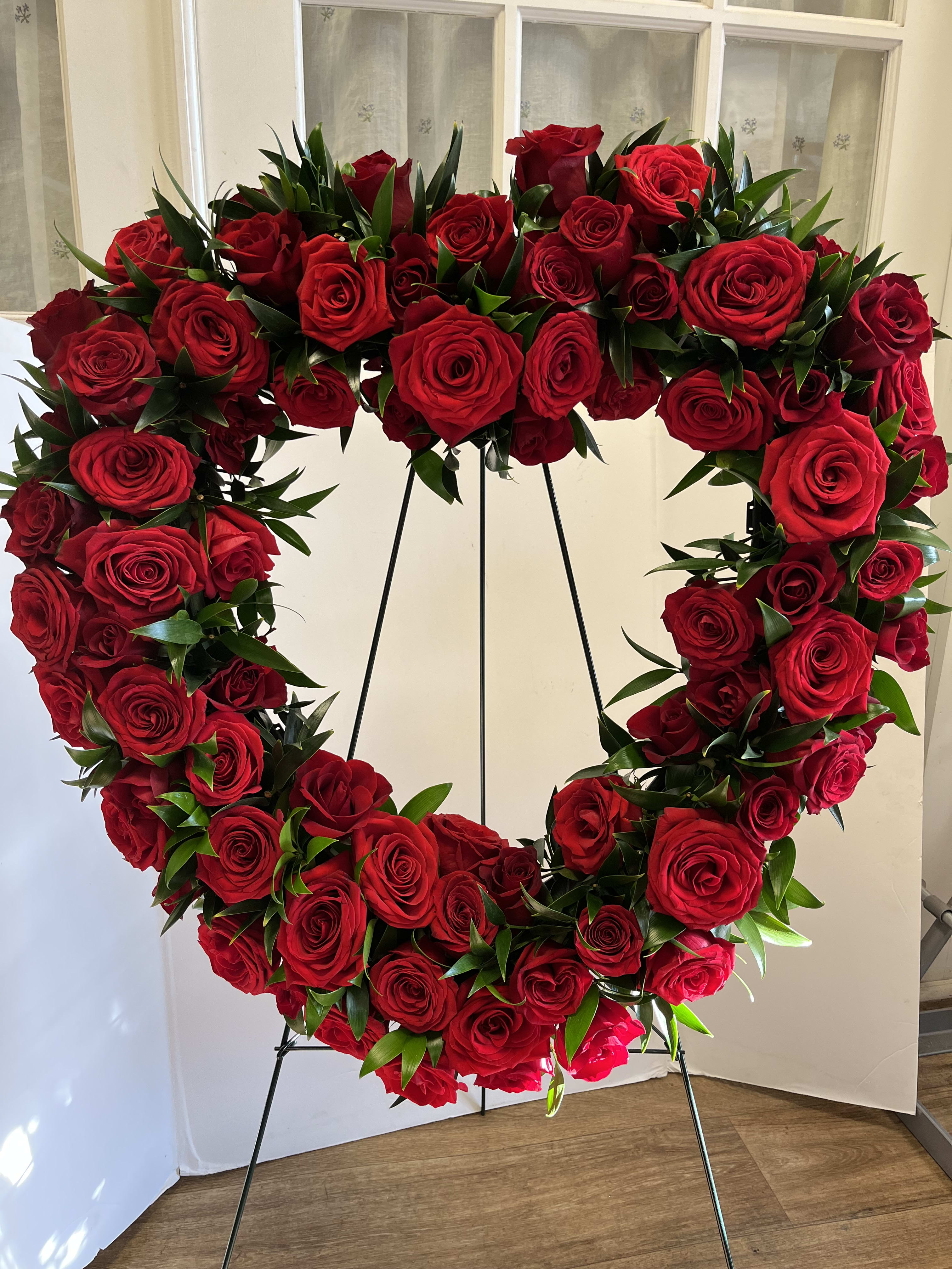 Heart-shaped wreath of red roses on a black stand