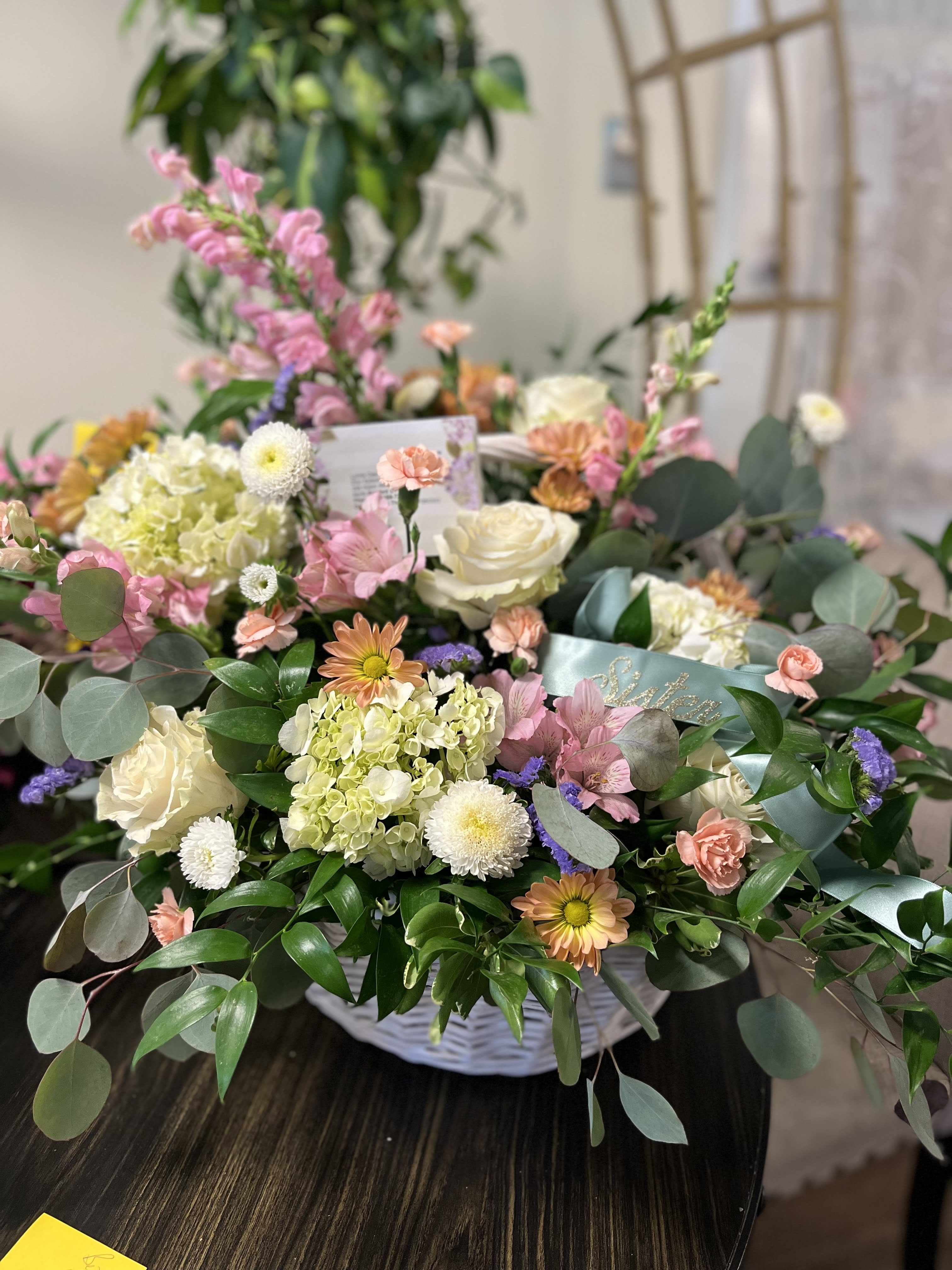 Mixed pastel flower arrangement in a white basket with roses and chrysanthemums