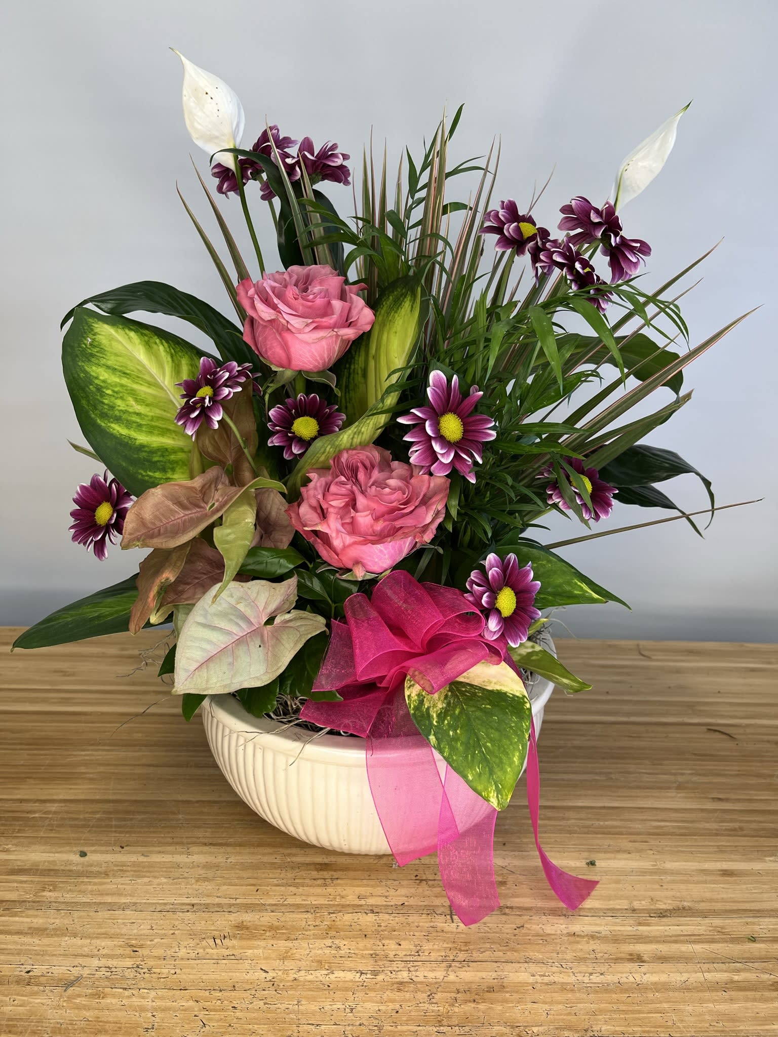 Pink roses and purple daisies in a white bowl vase with ribbon