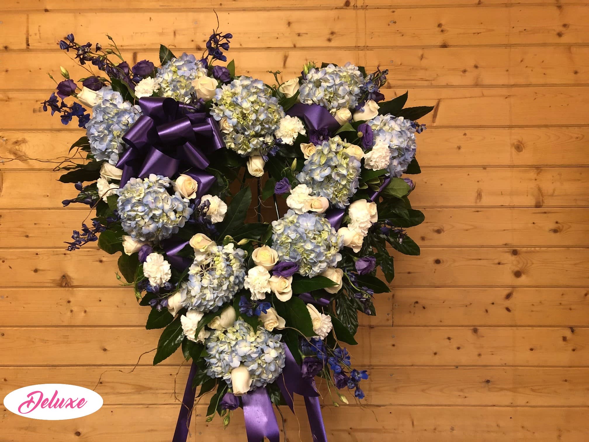 Heart-shaped floral wreath with blue hydrangeas, white roses, and purple ribbon