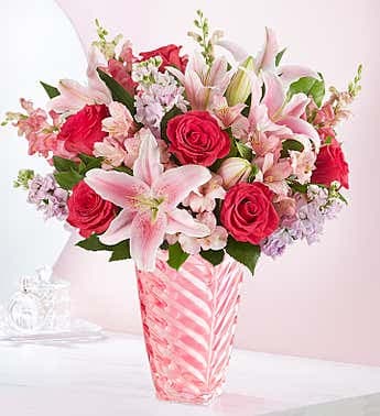 Pink and red bouquet of roses and lilies in a striped glass vase