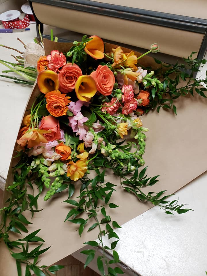 Bouquet of orange and pink flowers with trailing greenery on brown paper