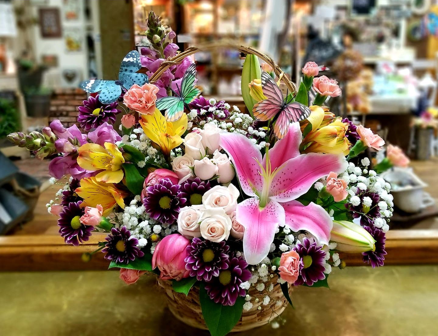Basket arrangement of pink lilies, roses, and purple daisies with butterfly picks