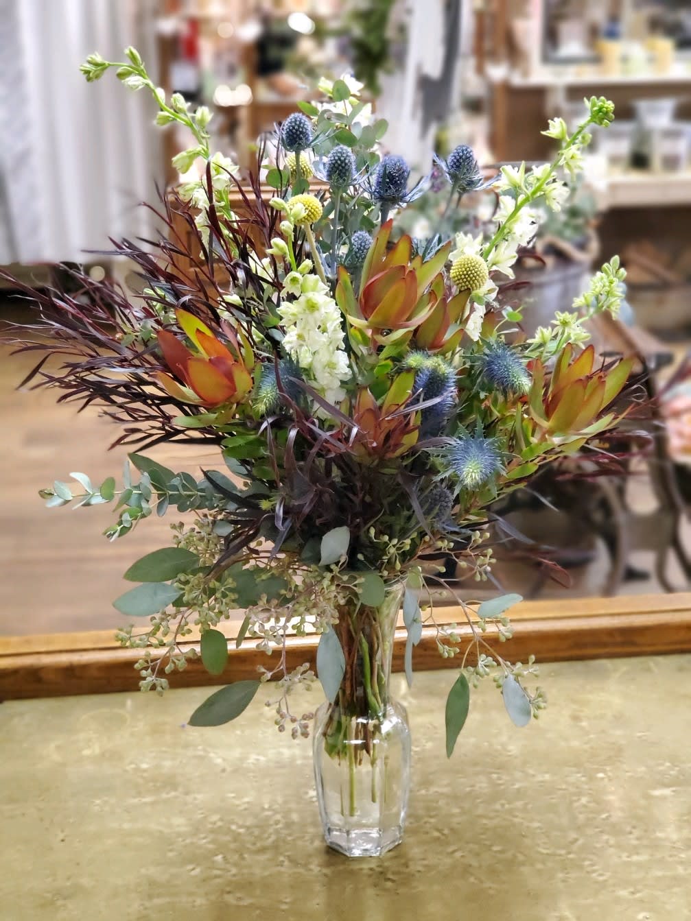 Mixed floral arrangement in a clear glass vase with blue thistle and orange protea
