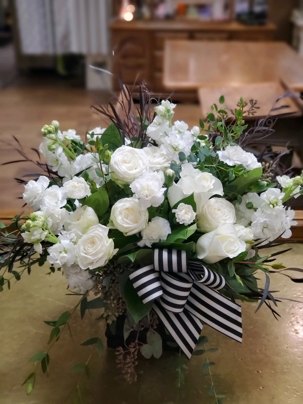 White floral arrangement with a striped ribbon in a low container