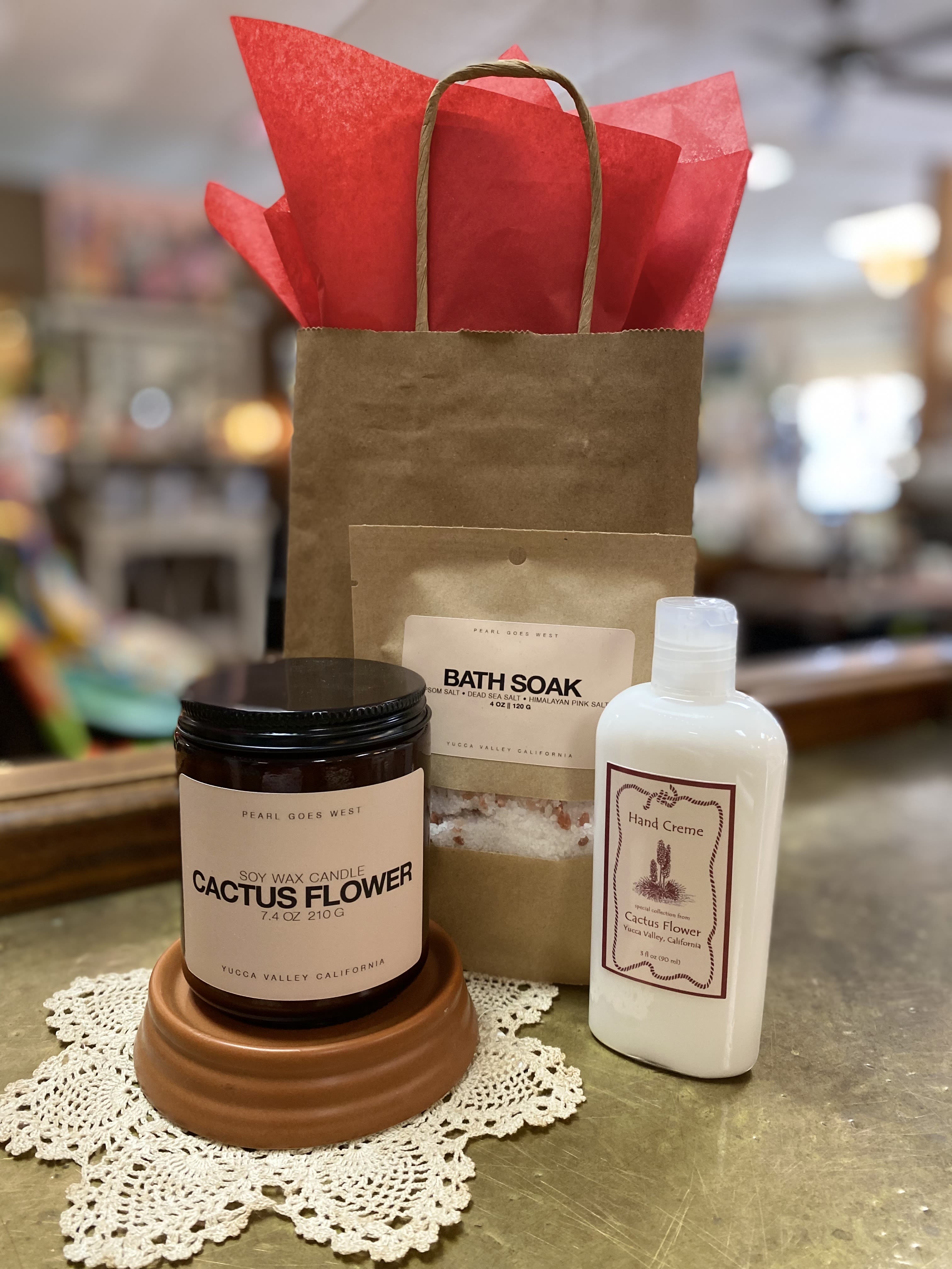 Gift set with cactus flower candle, bath soak, and hand cream beside a kraft gift bag with red tissue paper.