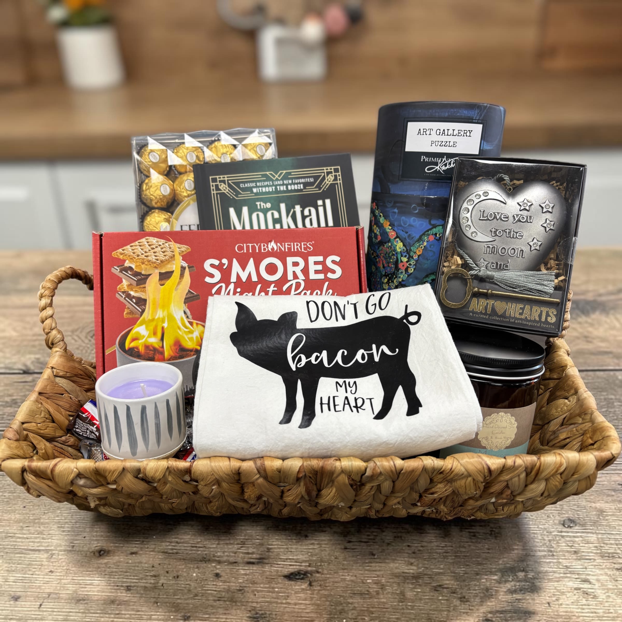 The Weekend In Gift Basket - A little fun with the Don't Go Bacon My Heart tea towel and the Love You To The Moon and Back Heart with key keepsake this basket has got you covered for a fun weekend in. We threw in a puzzle for some phone free face to face time and a fantastic counter top smores kit. Now all we need are those candles and chocolates and a mocktails recipe book and you're all set! All gathered up in a basket she's going to love!