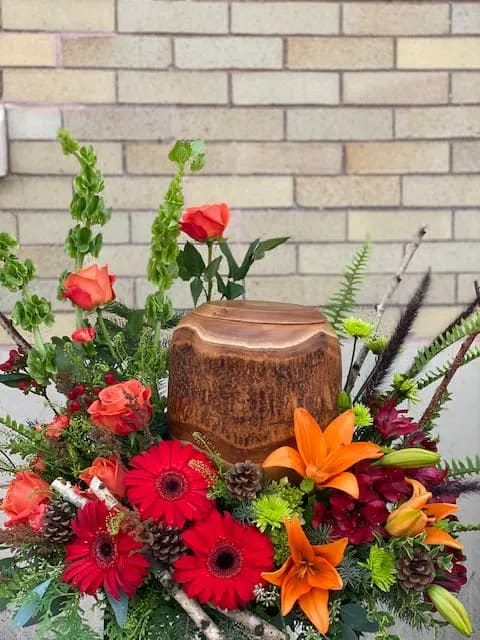 Bright mixed floral arrangement with roses, gerbera daisies, and lilies around a wooden urn