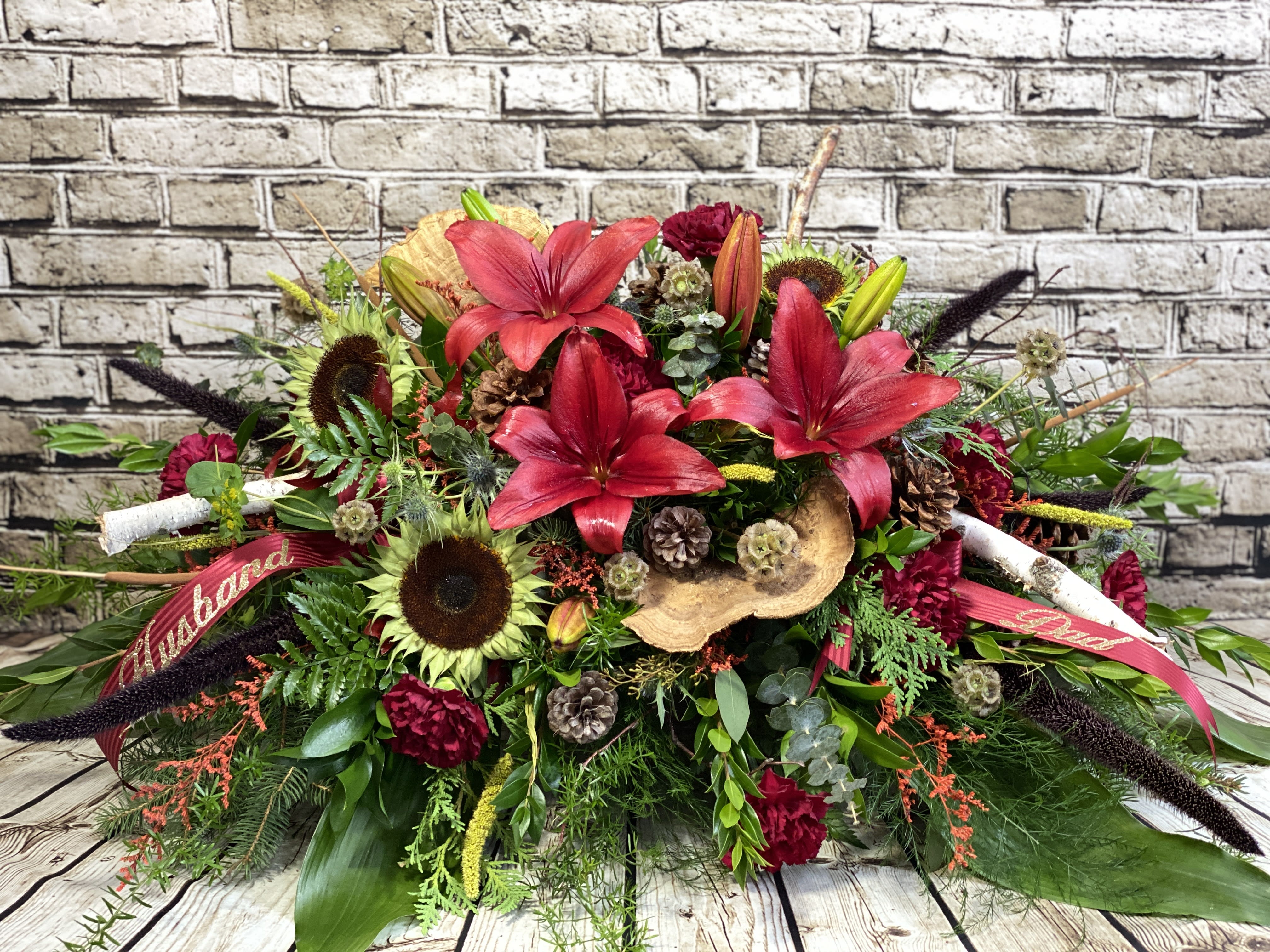 Large red floral arrangement with lilies and sunflowers, accented by ribbons