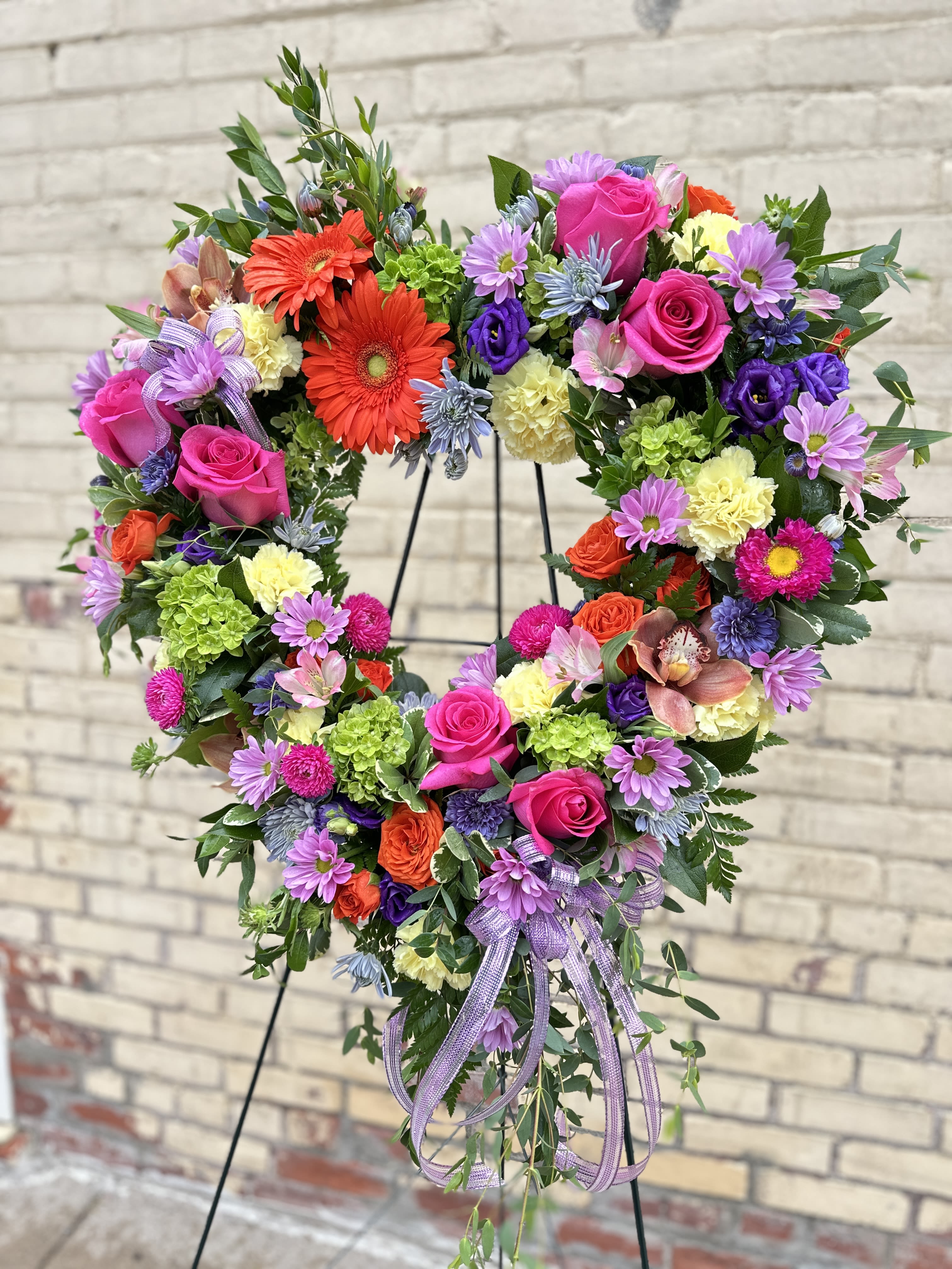 Heart-shaped floral wreath with pink roses and purple daisies on a stand