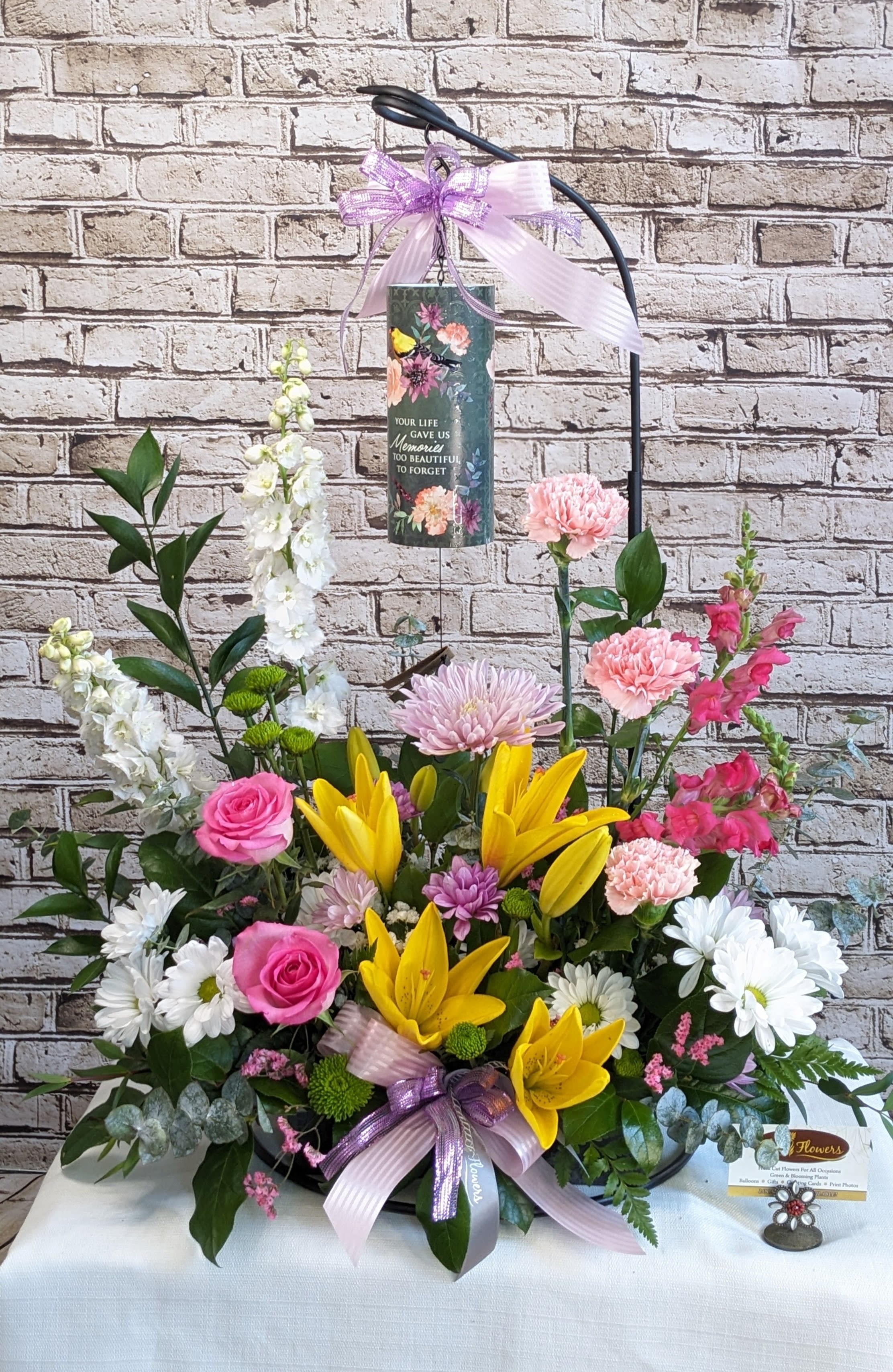 Standing floral tribute with lilies, roses, and daisies around a memorial plaque