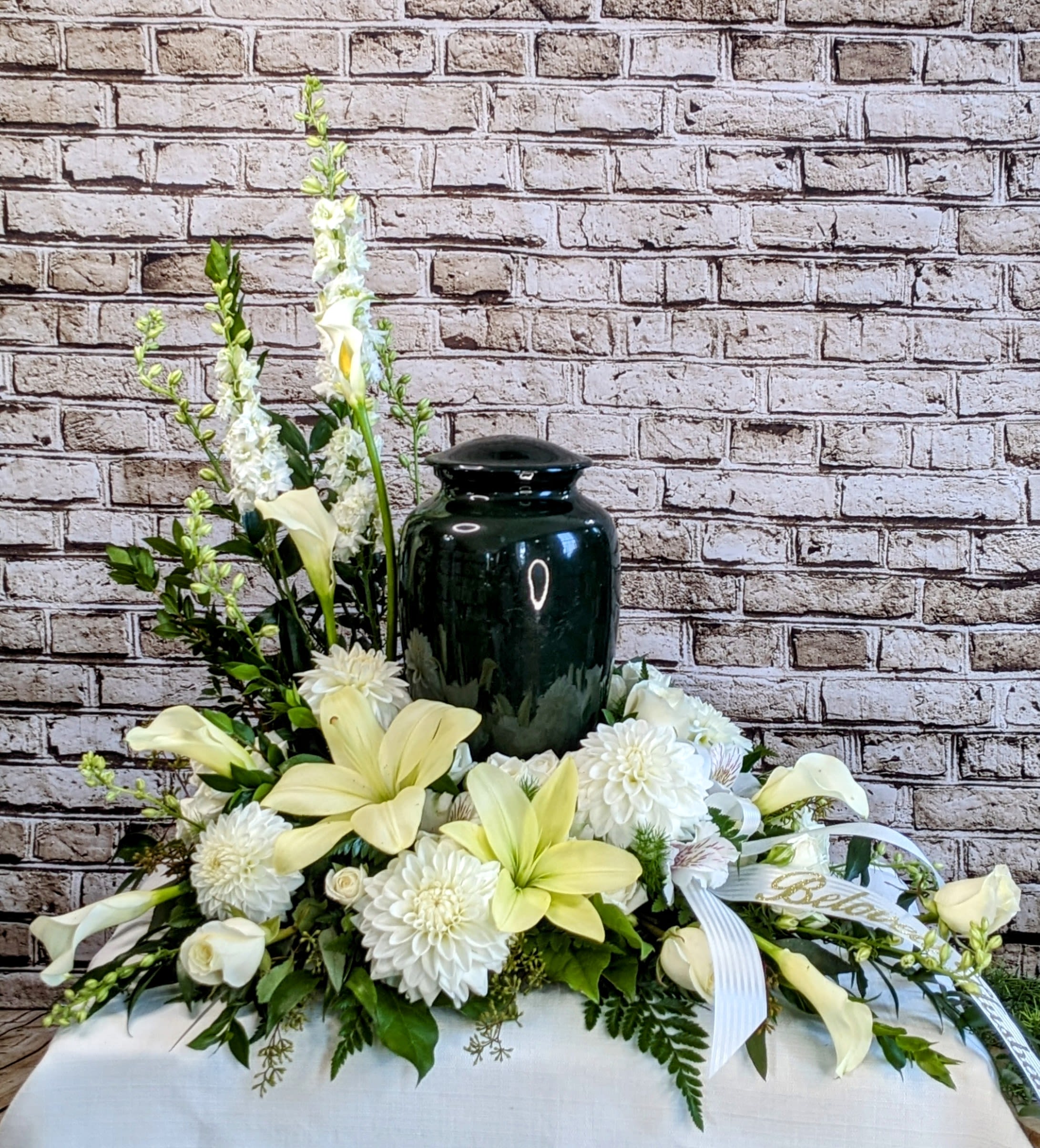 White floral arrangement with a dark urn centerpiece and ribbon accents