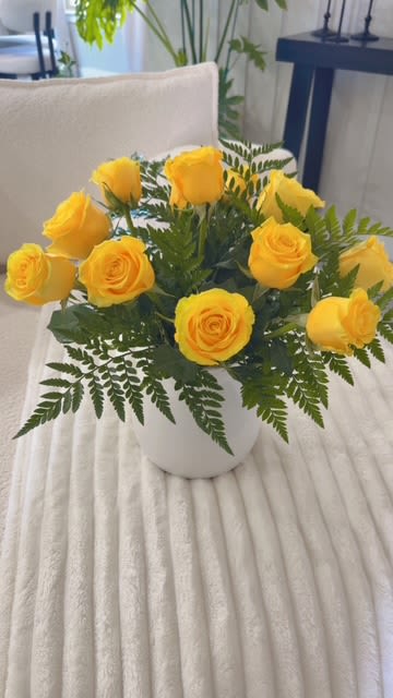 Yellow roses arranged in a white vase with fern foliage