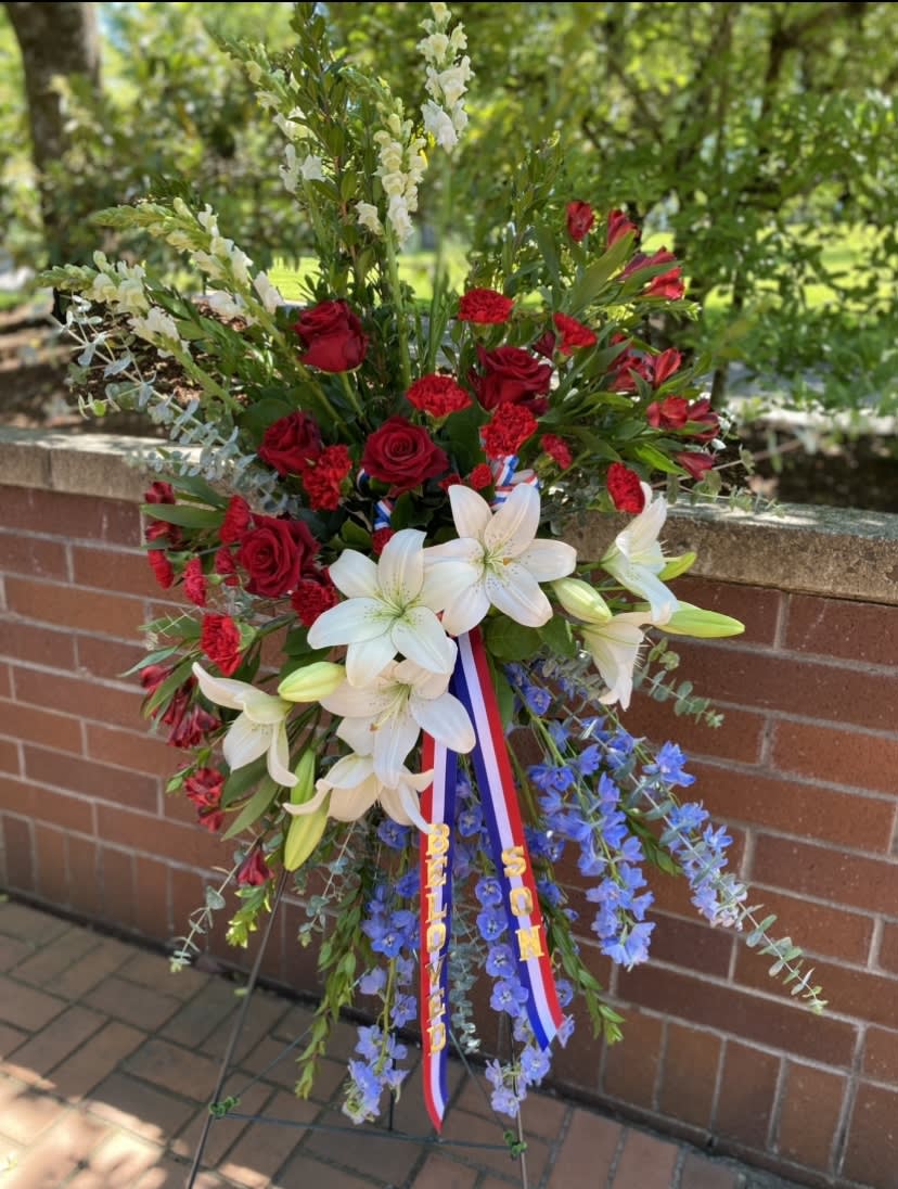 Standing floral spray with red roses, white lilies, and blue flowers