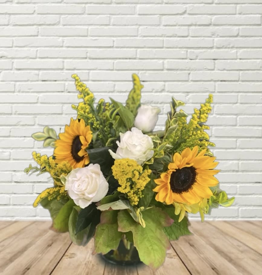 Sunflowers and white roses in a glass vase with yellow filler flowers