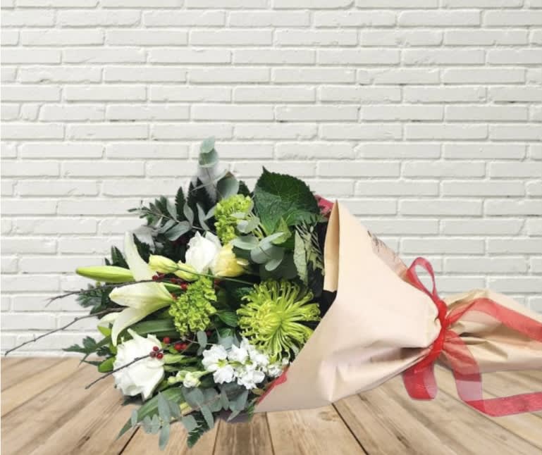 Bouquet of white lilies and green chrysanthemums wrapped in beige paper with a red ribbon