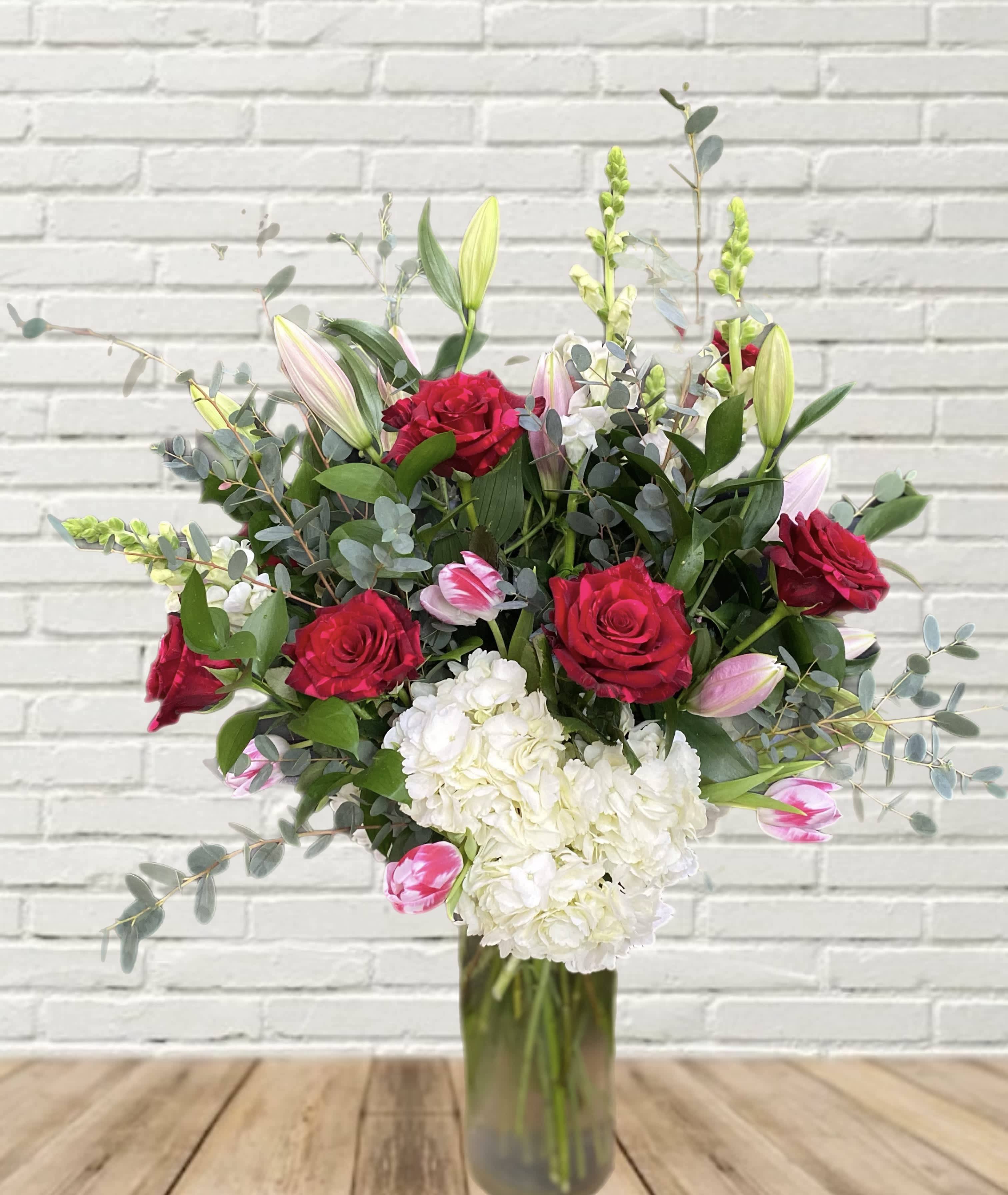 Bouquet of red roses, white hydrangea, and pink tulips in a glass vase