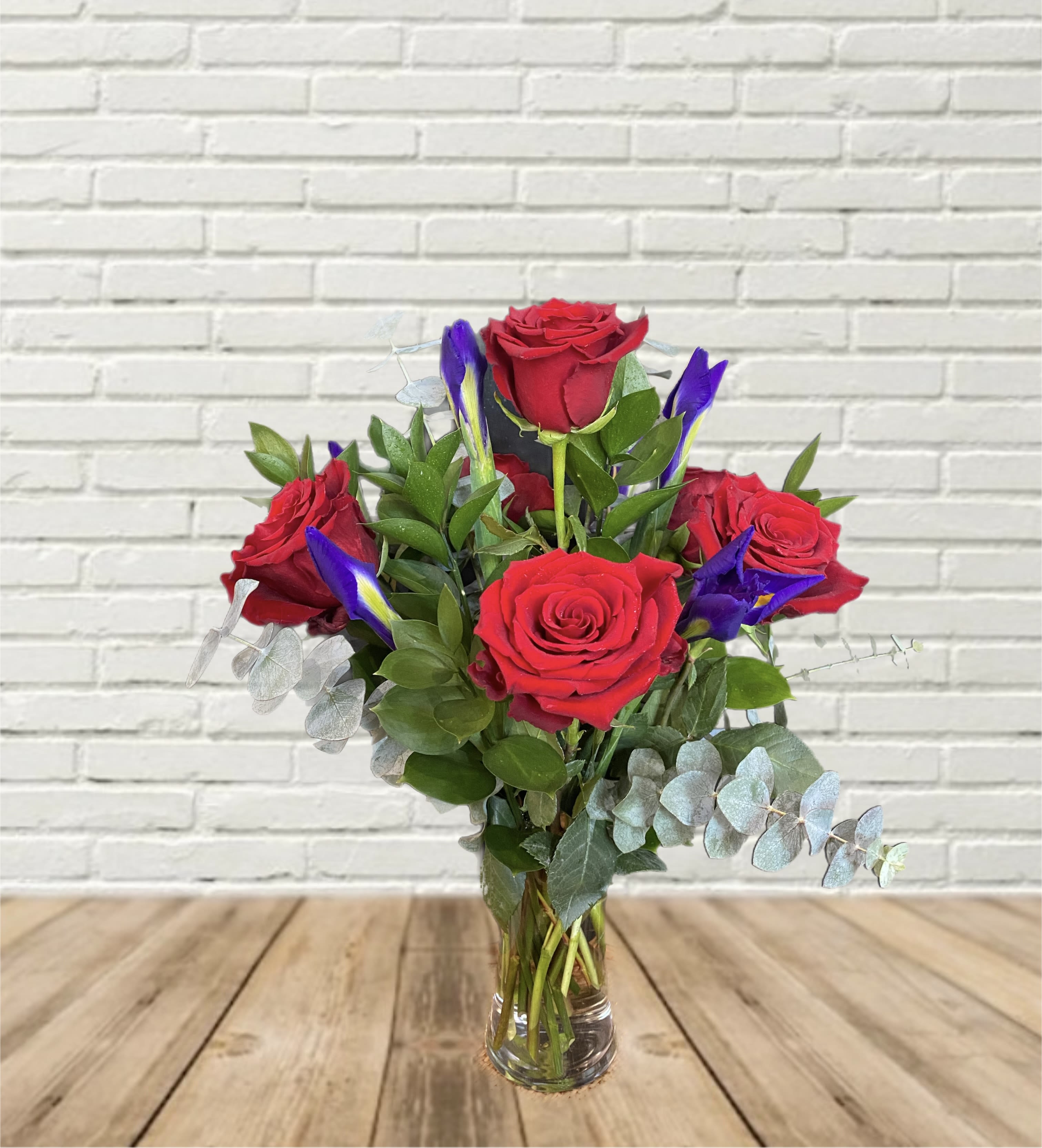 Red roses and purple iris in a clear glass vase
