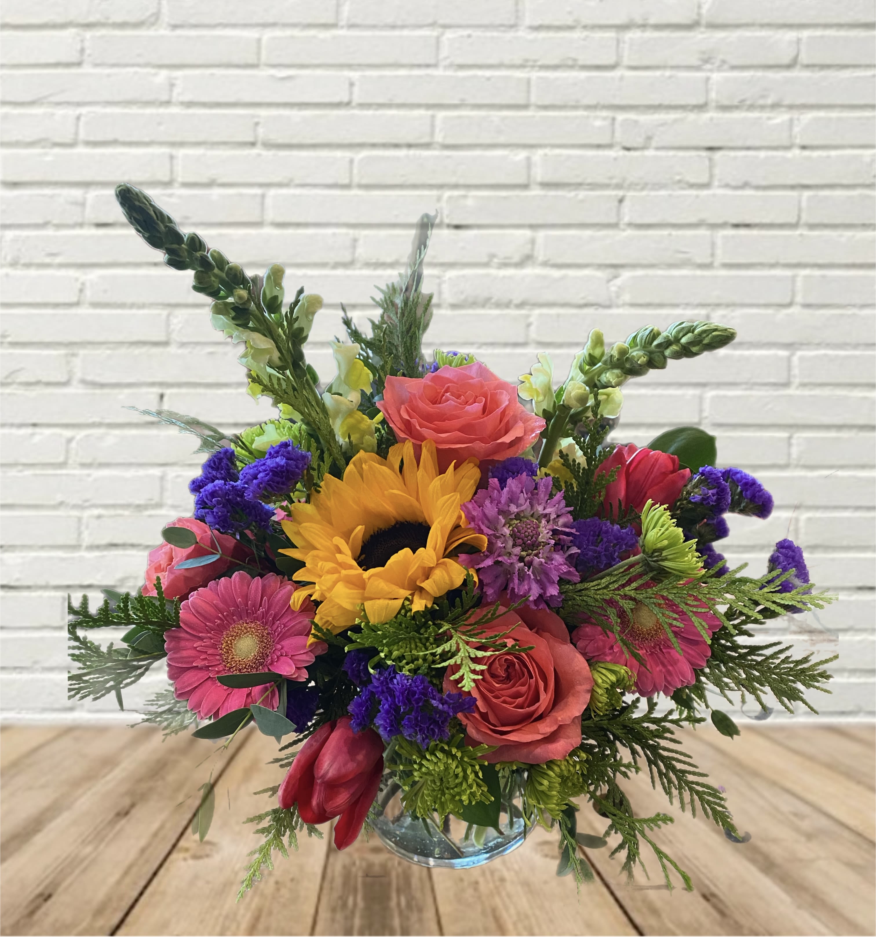 Colorful bouquet with sunflowers, roses, and gerbera daisies in a glass vase