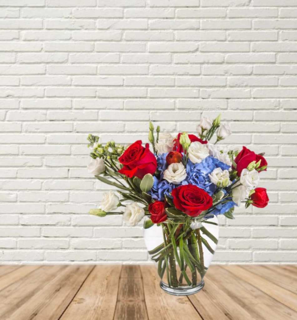 Bouquet of red roses, blue hydrangeas, and white blooms in a glass vase