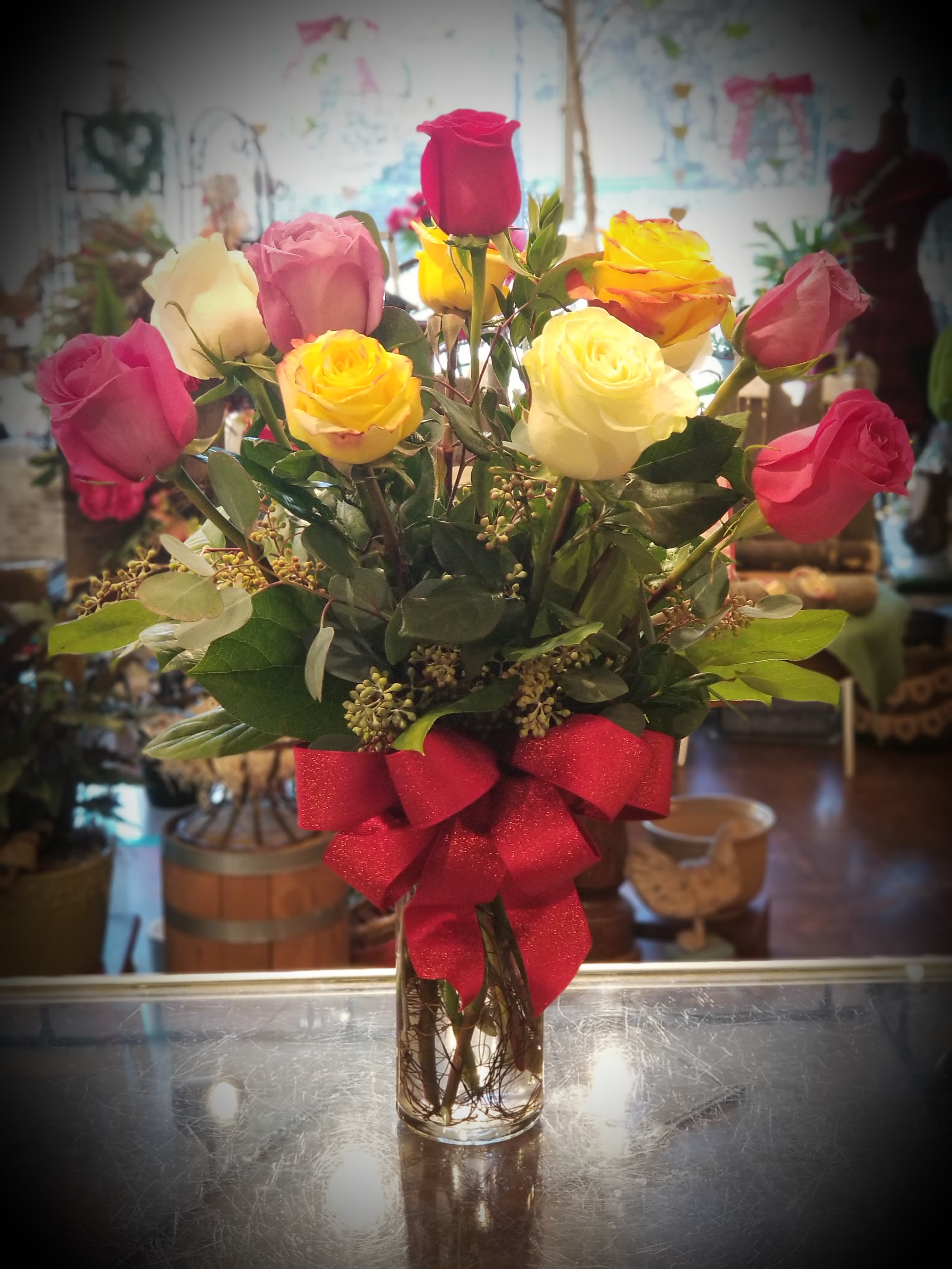 Bouquet of multicolored roses in a clear glass vase with a red bow