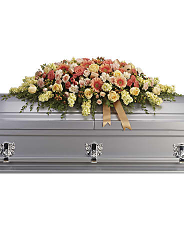 Large floral spray on a silver casket with peach and cream flowers