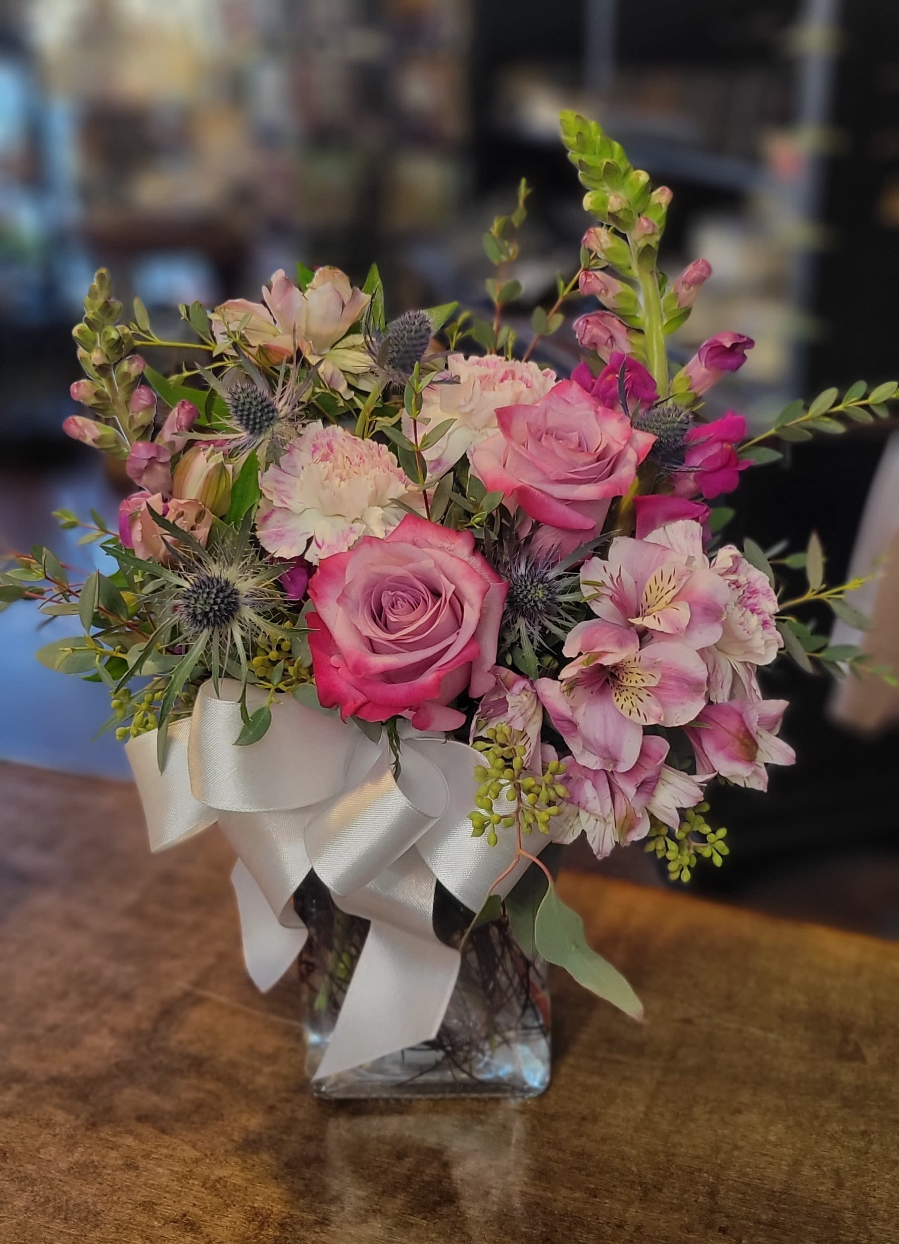 Pink roses and mixed blooms arranged in a glass vase with a white ribbon