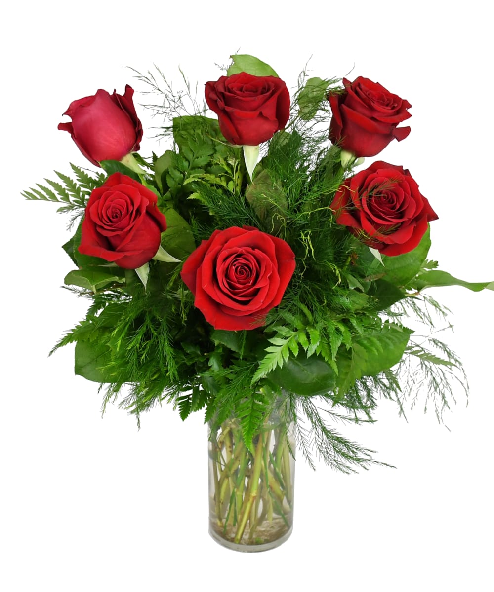 Red roses arranged in a clear glass vase with green foliage