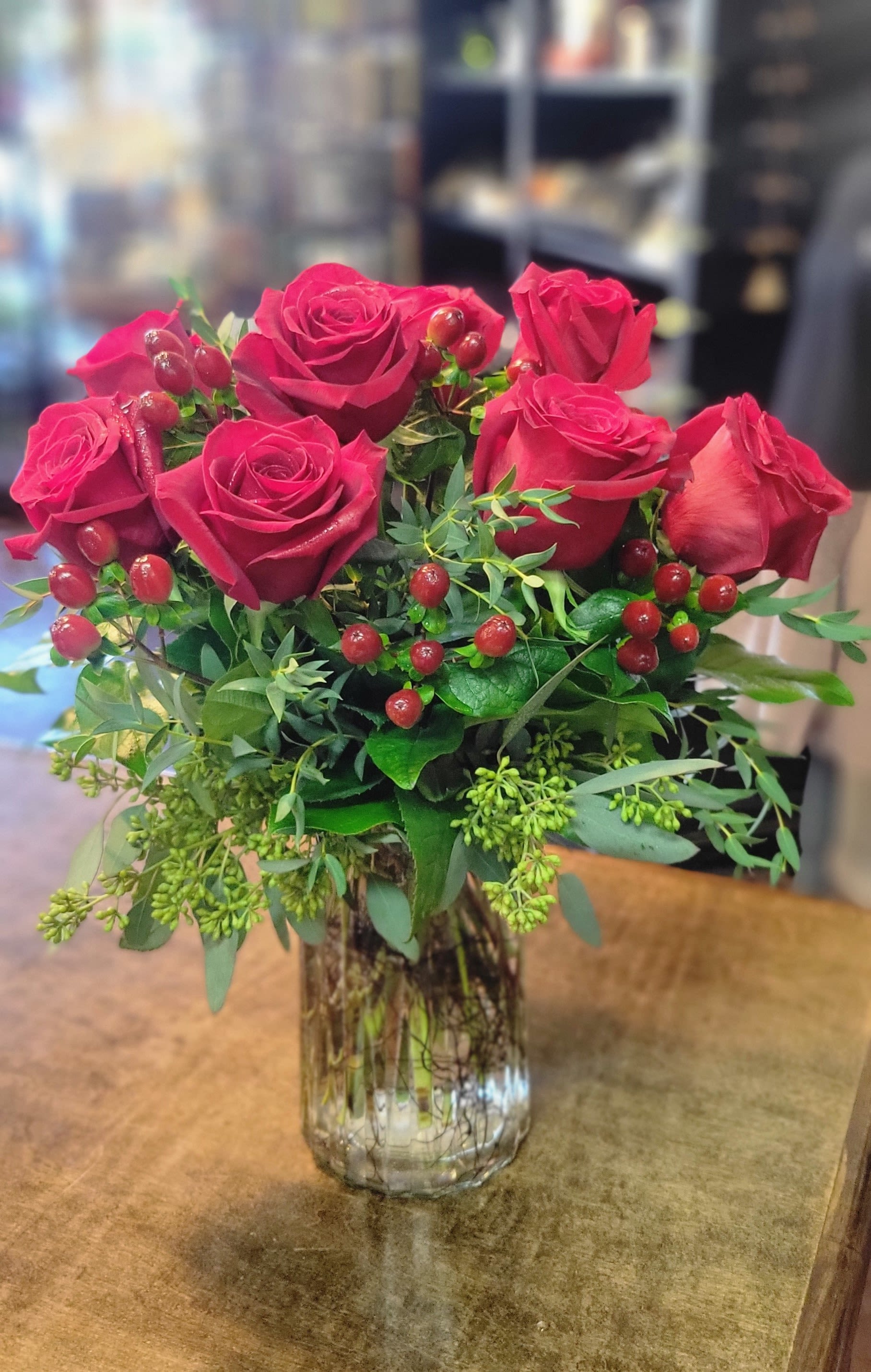 Red roses arranged in a clear glass vase with berry accents