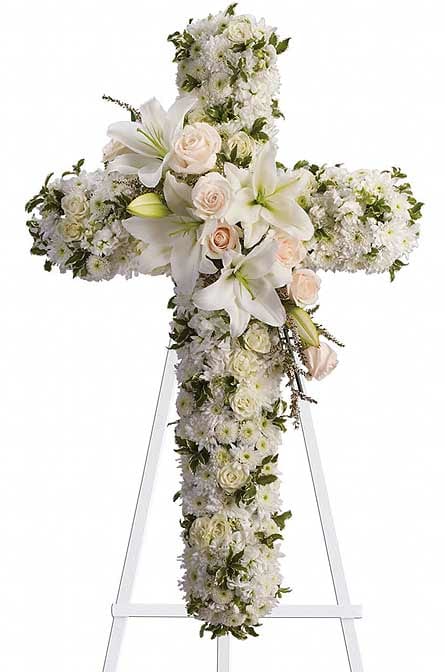 White floral cross on a stand with lilies and roses