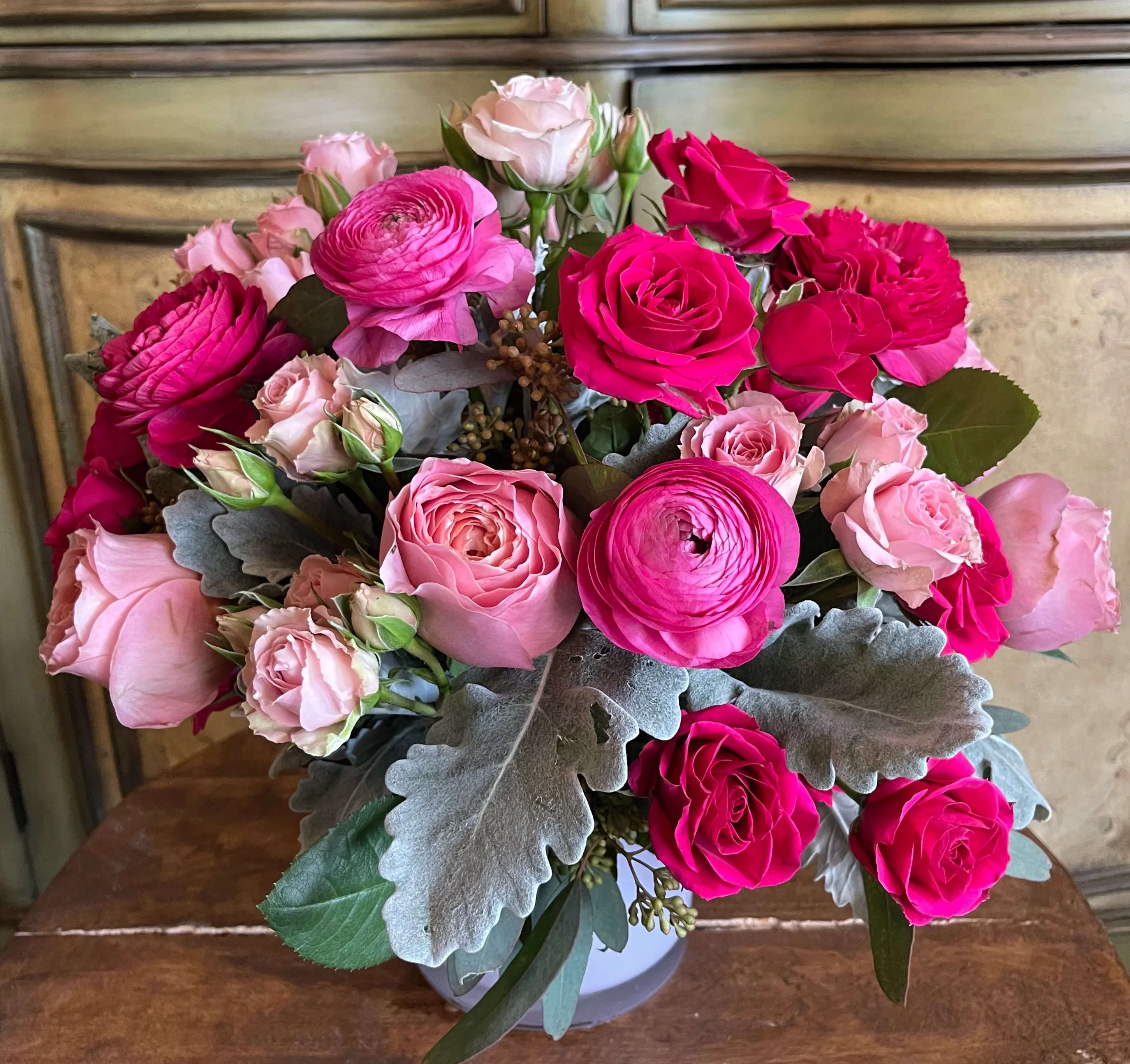 Pink and hot pink roses with ranunculus in a white vase